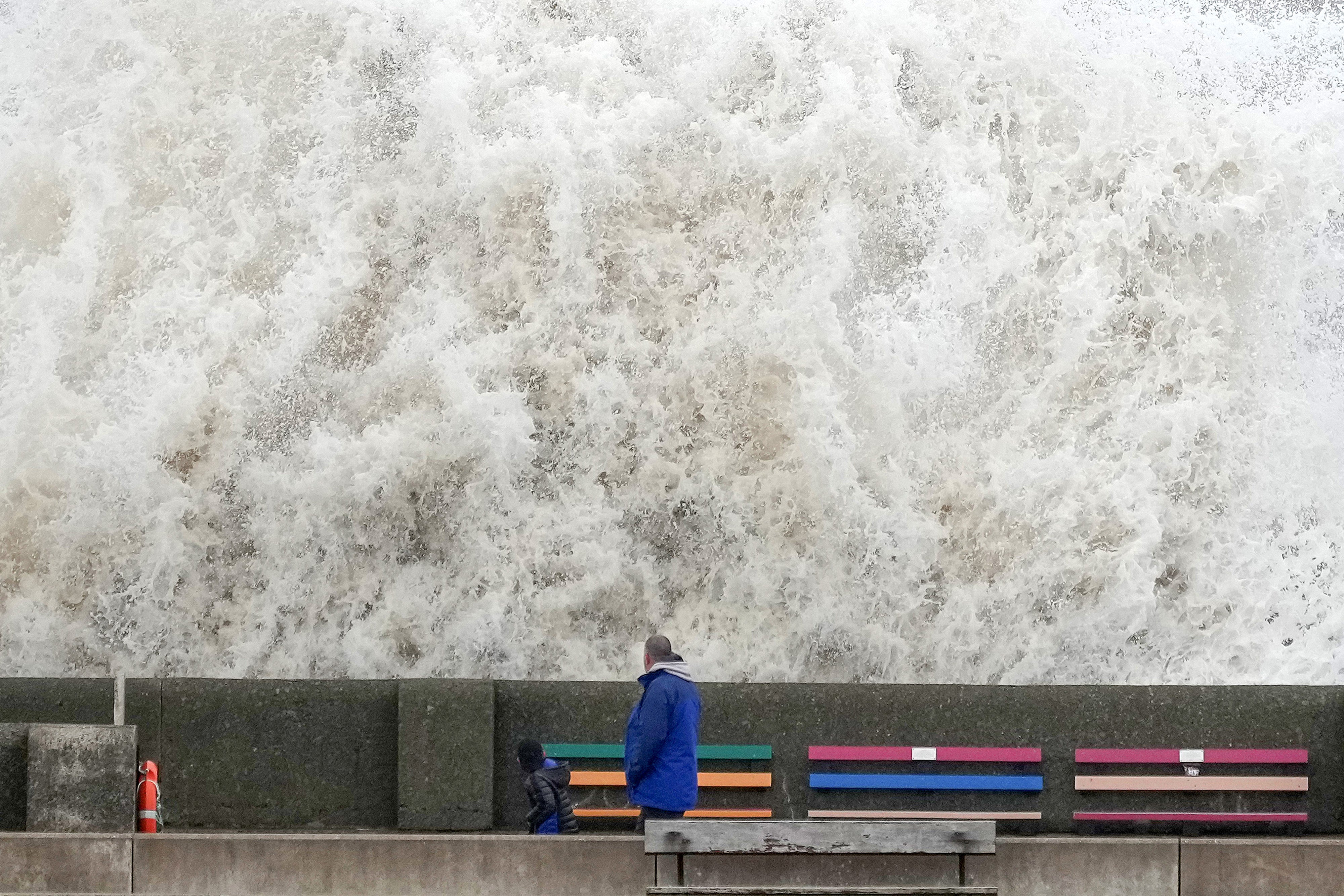 People view the waves created by high winds and spring tides hitting the sea wall at New Brighton promenade