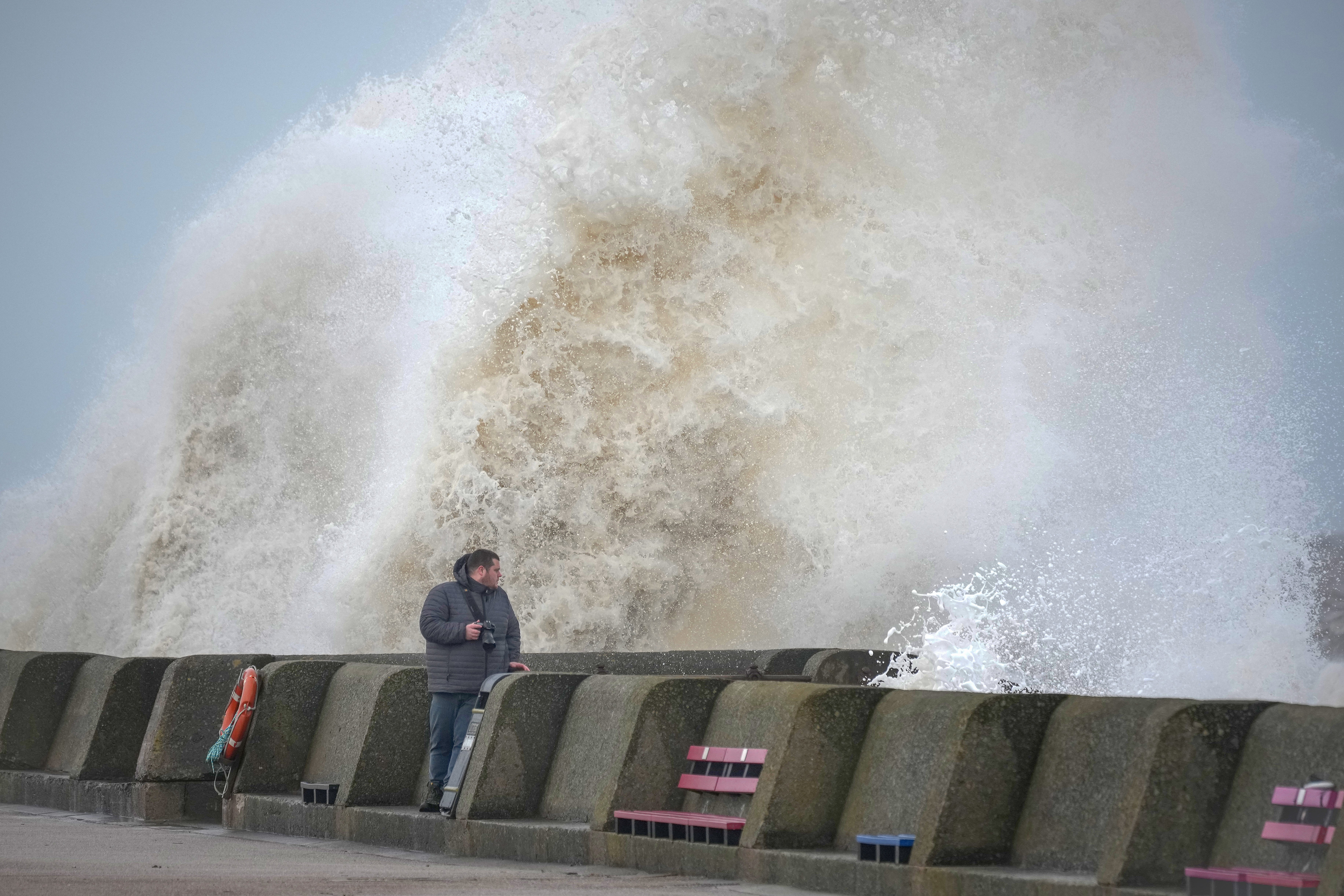 eople view the waves created by high winds and spring tides hitting the sea wall at New Brighton promenade