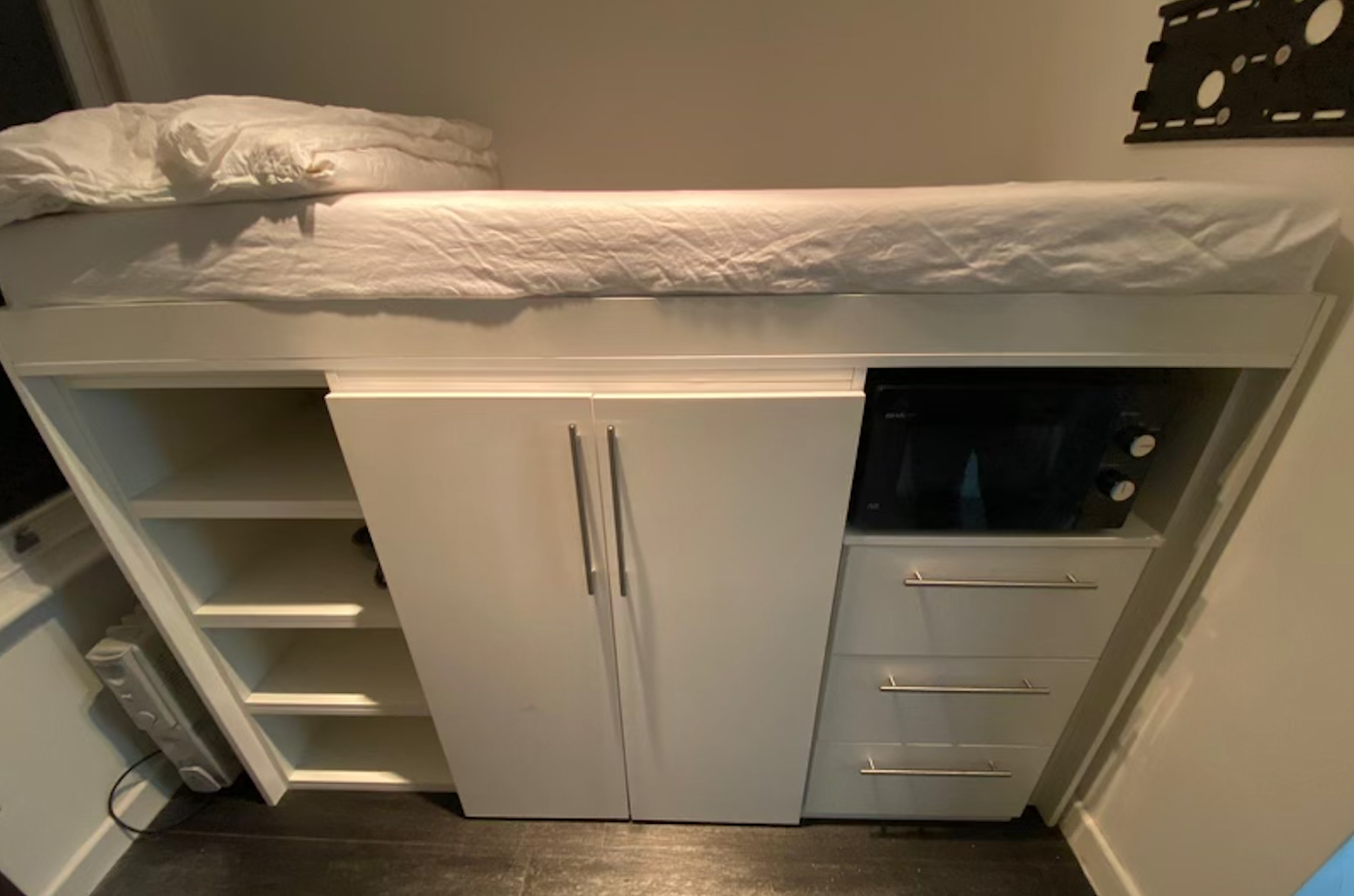 The bed is on top of storage space and a microwave