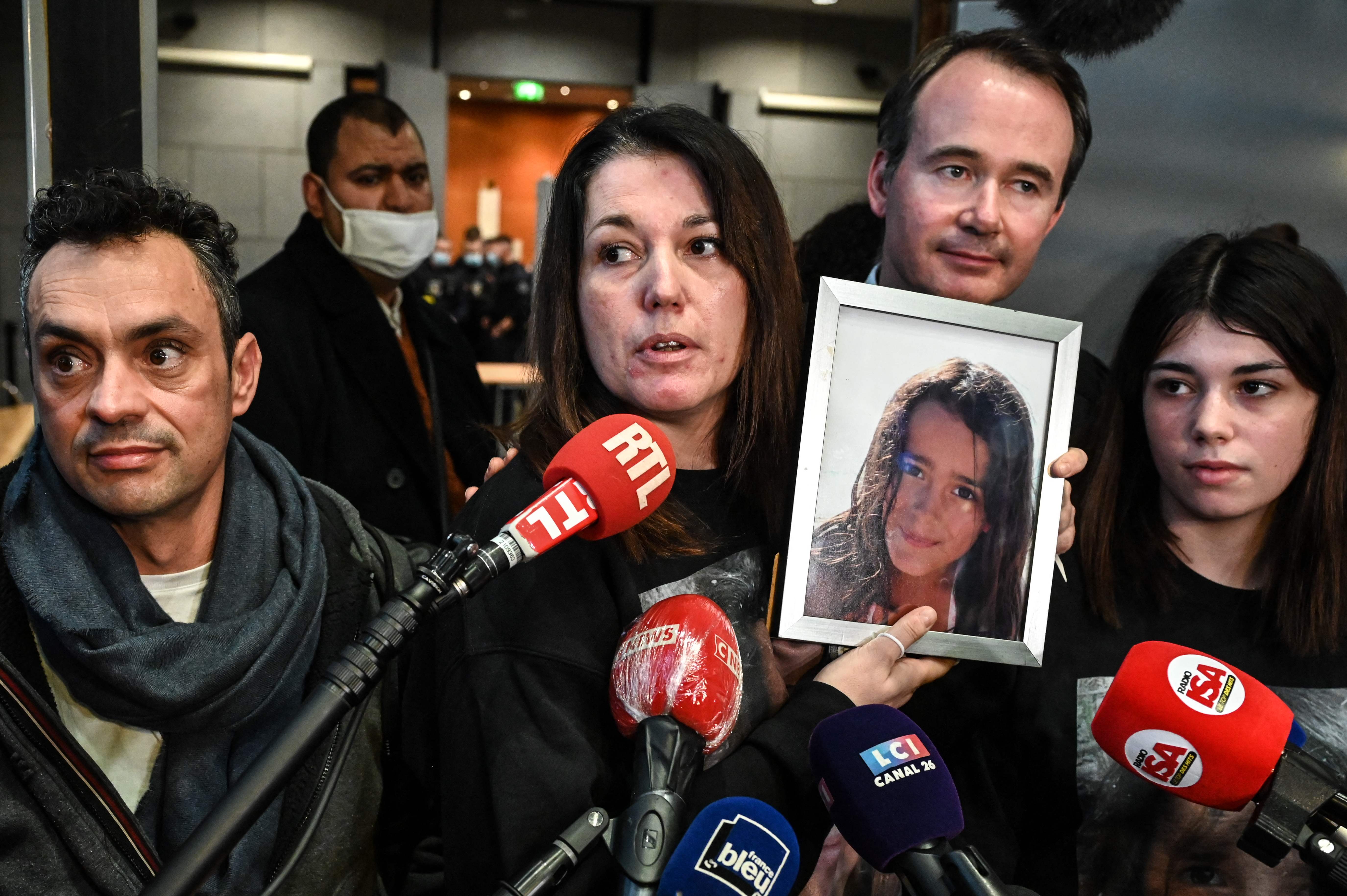 Jennifer Cleyet-Marrel holds a photo of her daughter outside the court, with Maelys’s father Joachim, sister Colleen and lawyer Fabien Rajon