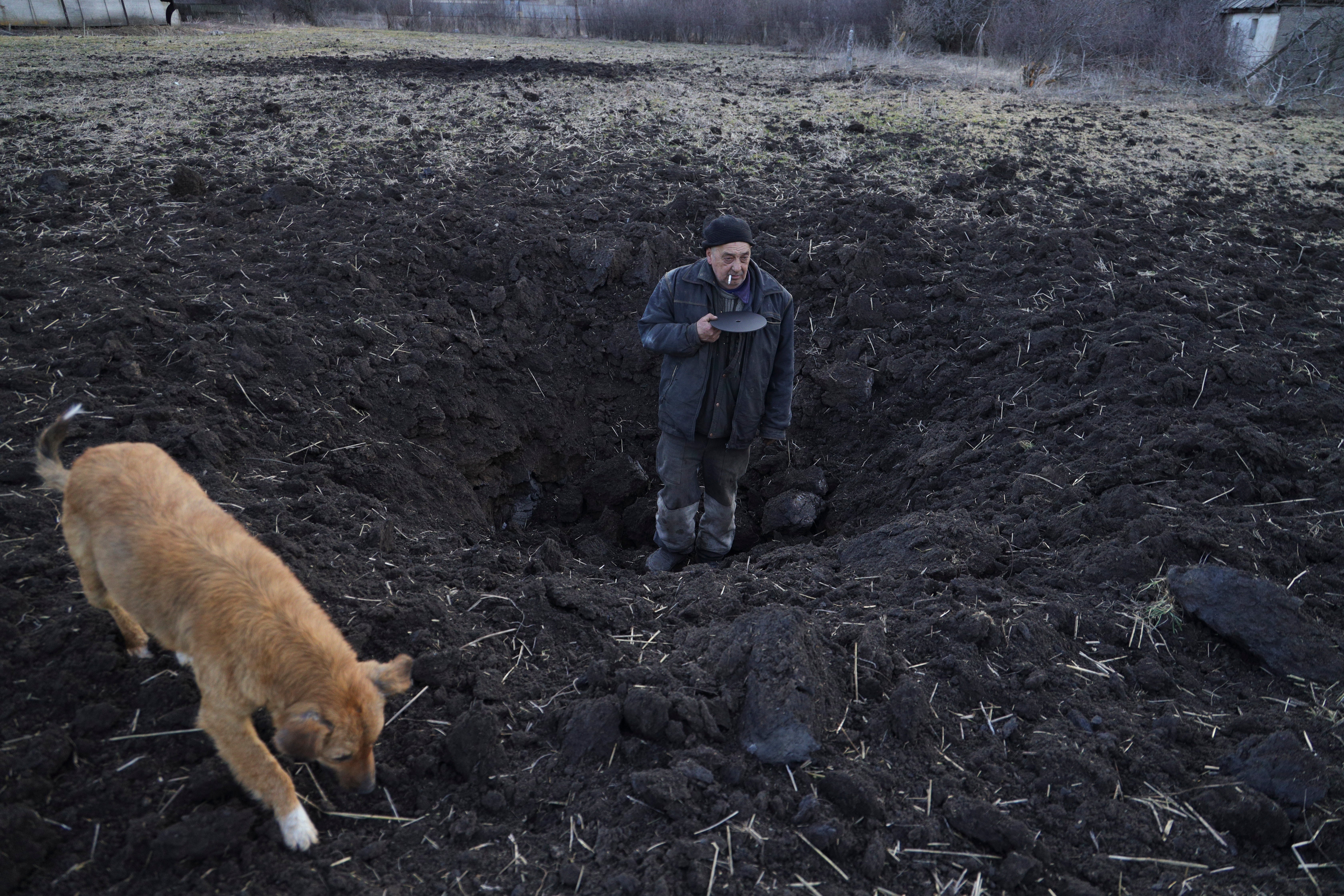 Local resident Valery shows the depth of the shell hole from the last shelling which took place in a field behind his house in a village near separatist-held city of Donetsk