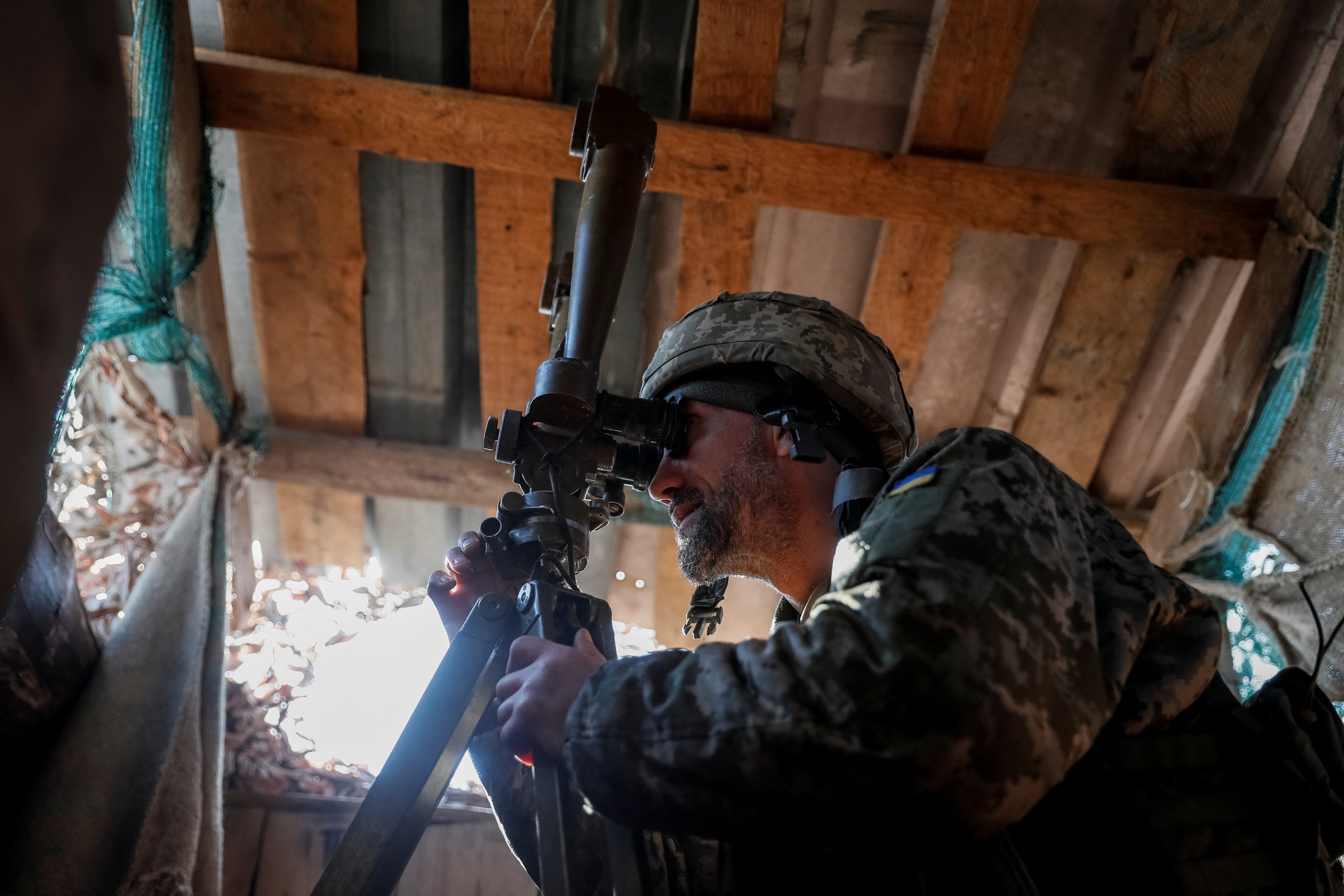 A Ukrainian service member uses a periscope while observing the area at a position on the frontline near the village of Travneve in Donetsk region