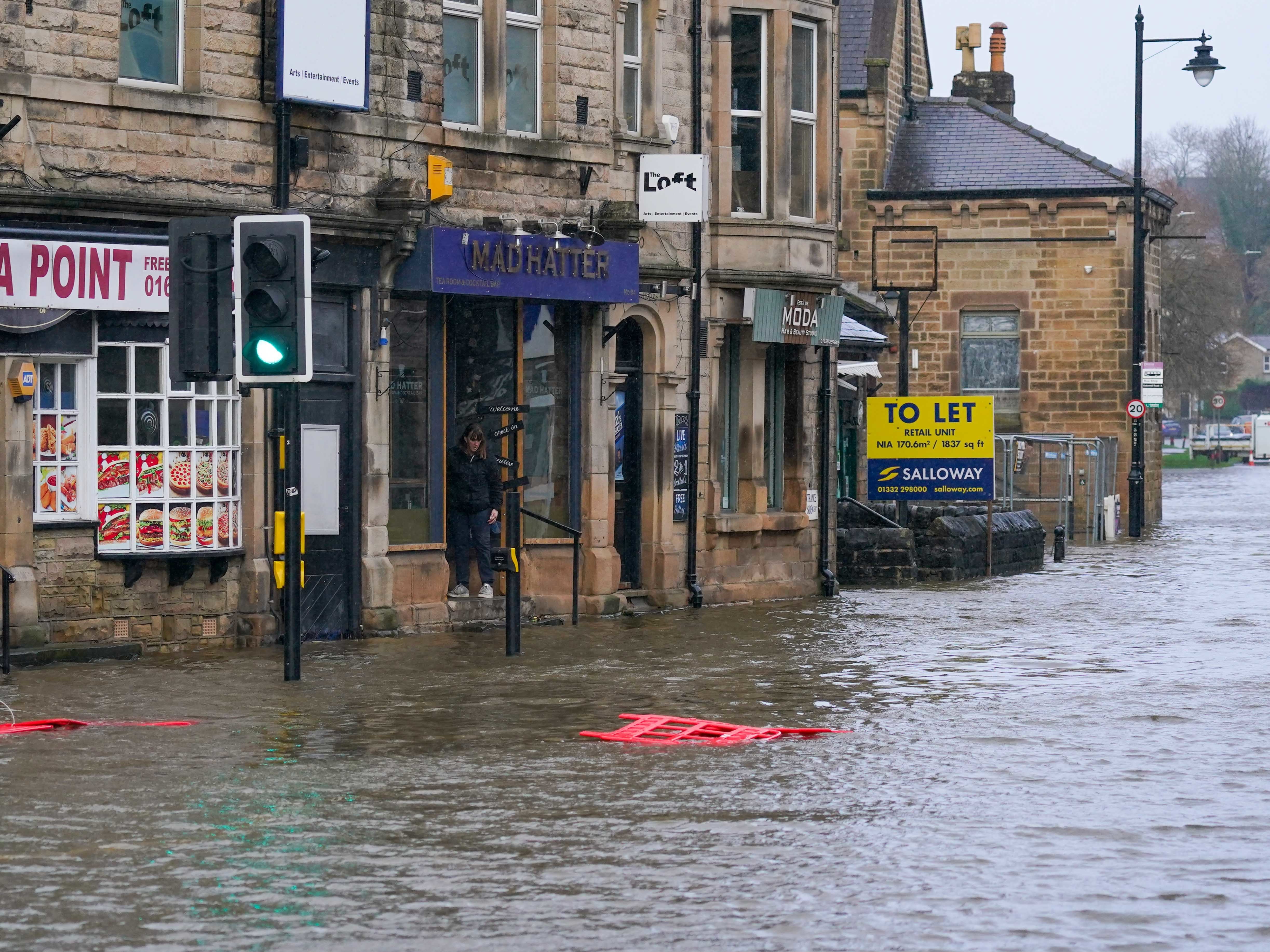 A person in a shop doorway surveys the flooded Bakewell Road in Matlock, Derbyshire