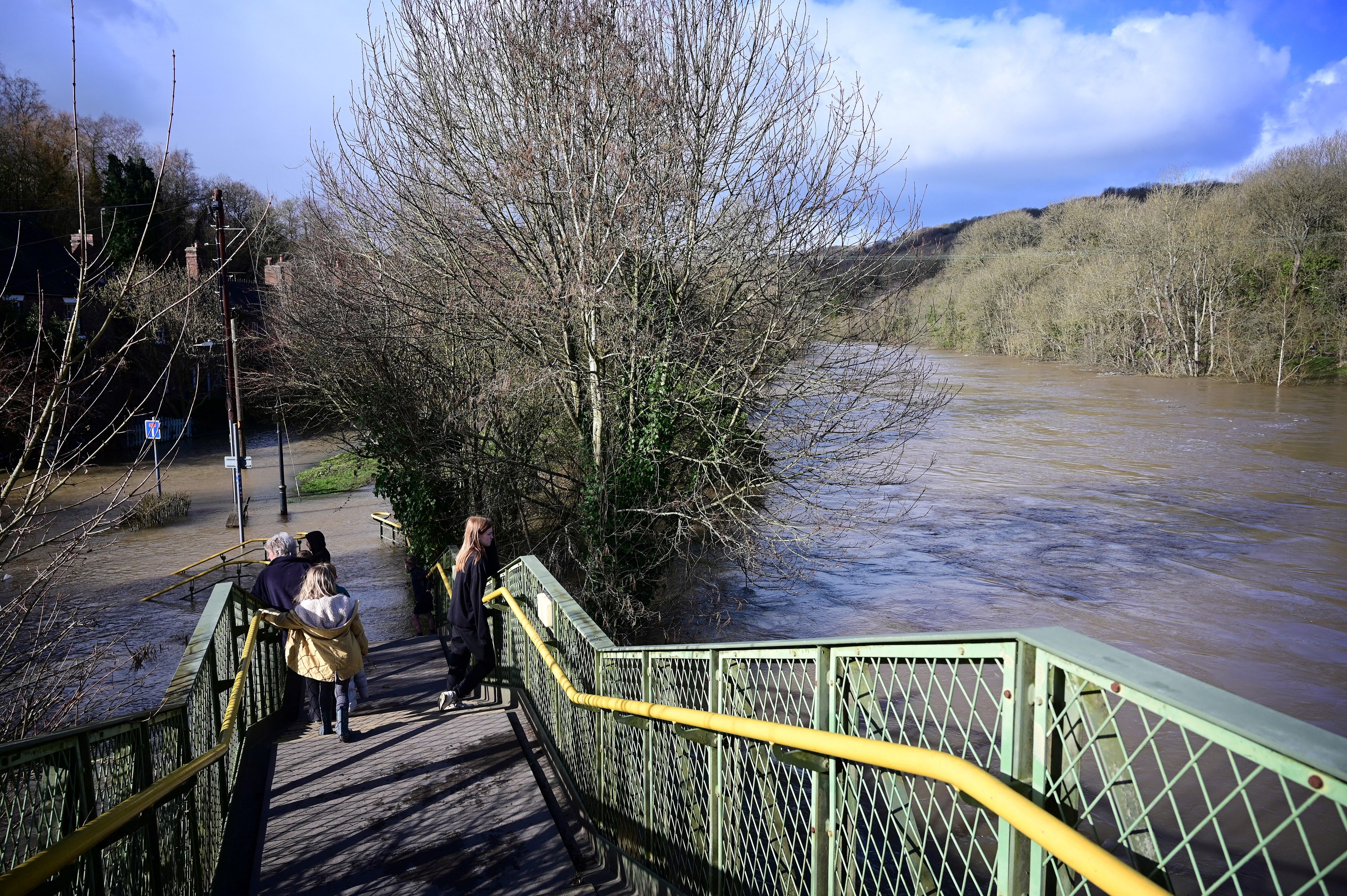 People stand on a footbridge to look at flood water after the River Severn burst its banks at Jackfield, near Telford, in central England on 22 February 2022