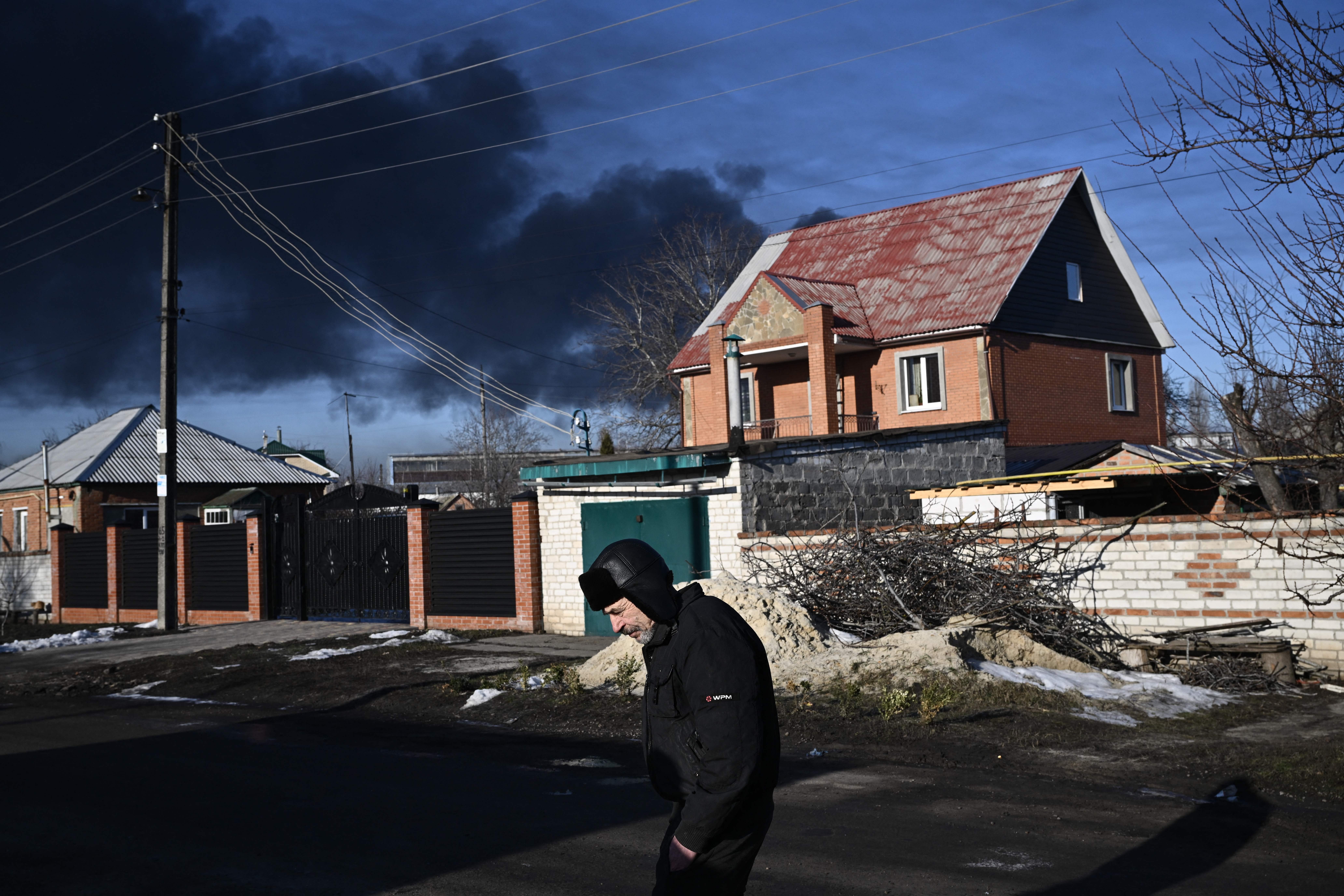 A man walks on a street as black smoke rises from a military airport in Chuguyev near Kharkiv on 24 February