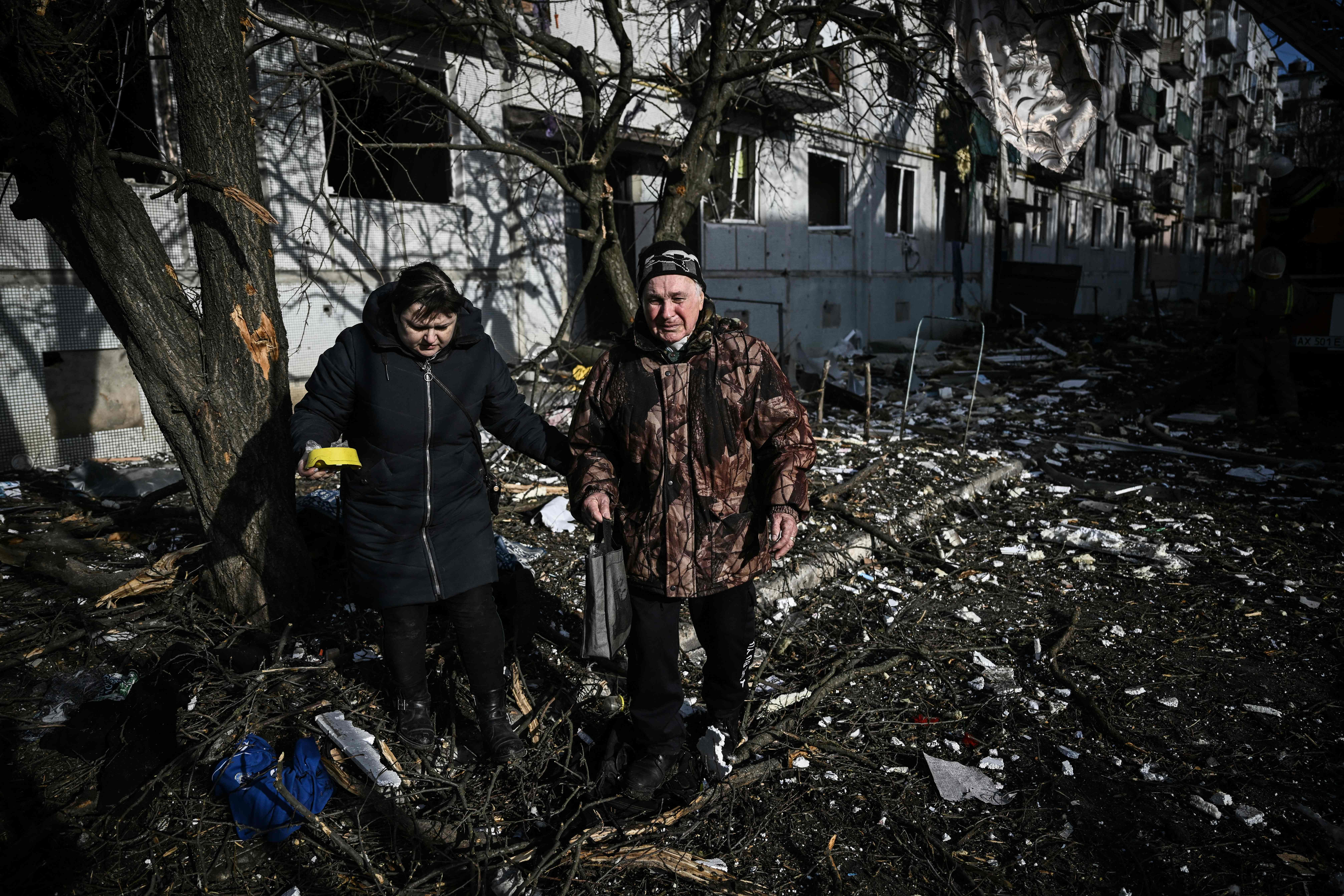 People walk past the body of a relative outside a destroyed building after bombings on the eastern Ukraine town of Chuguiv on 24 February 2022