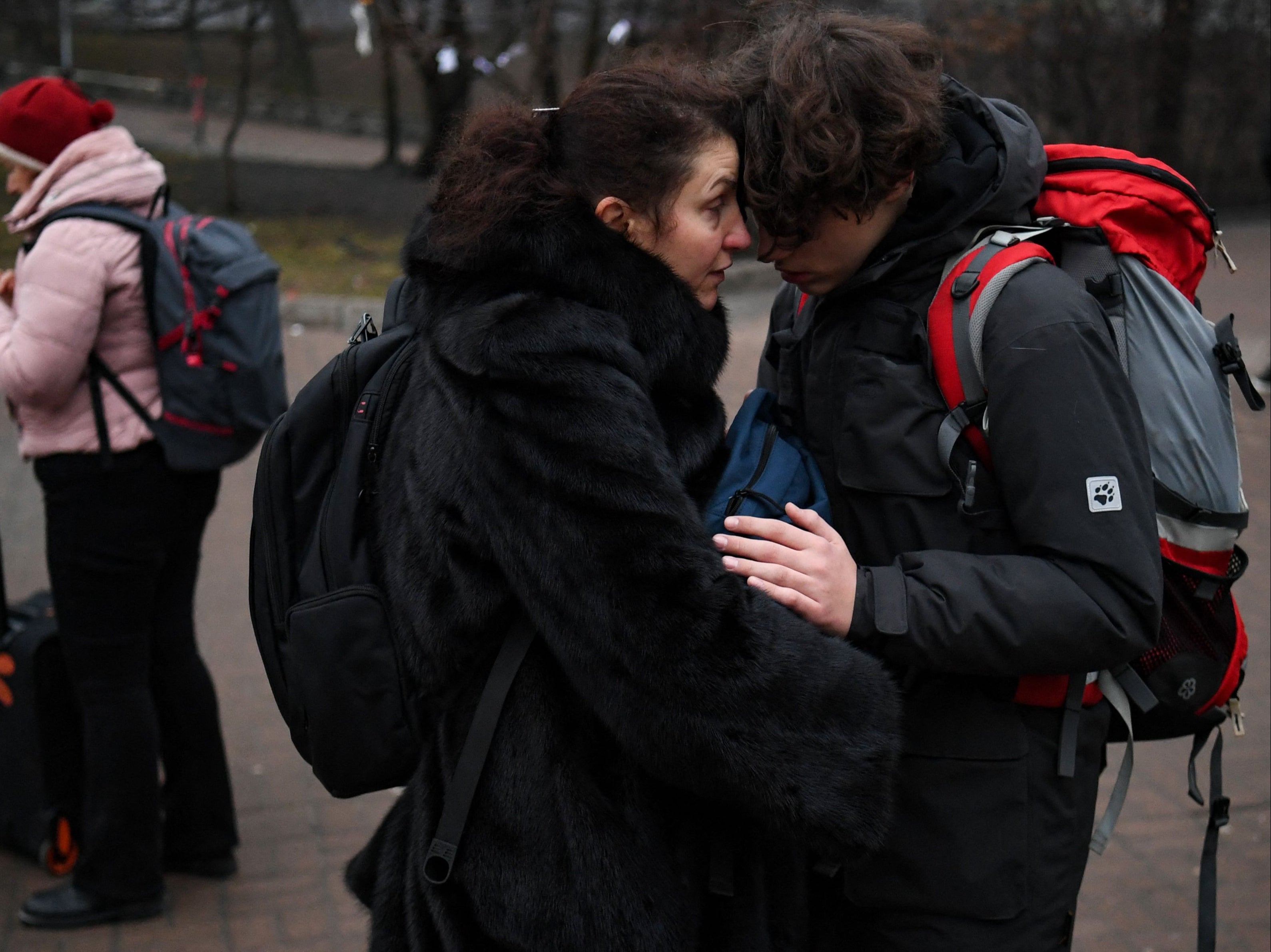 People hug as a woman with a suitcase uses her smartphone outside a metro station in Kiev in the morning of 24 February