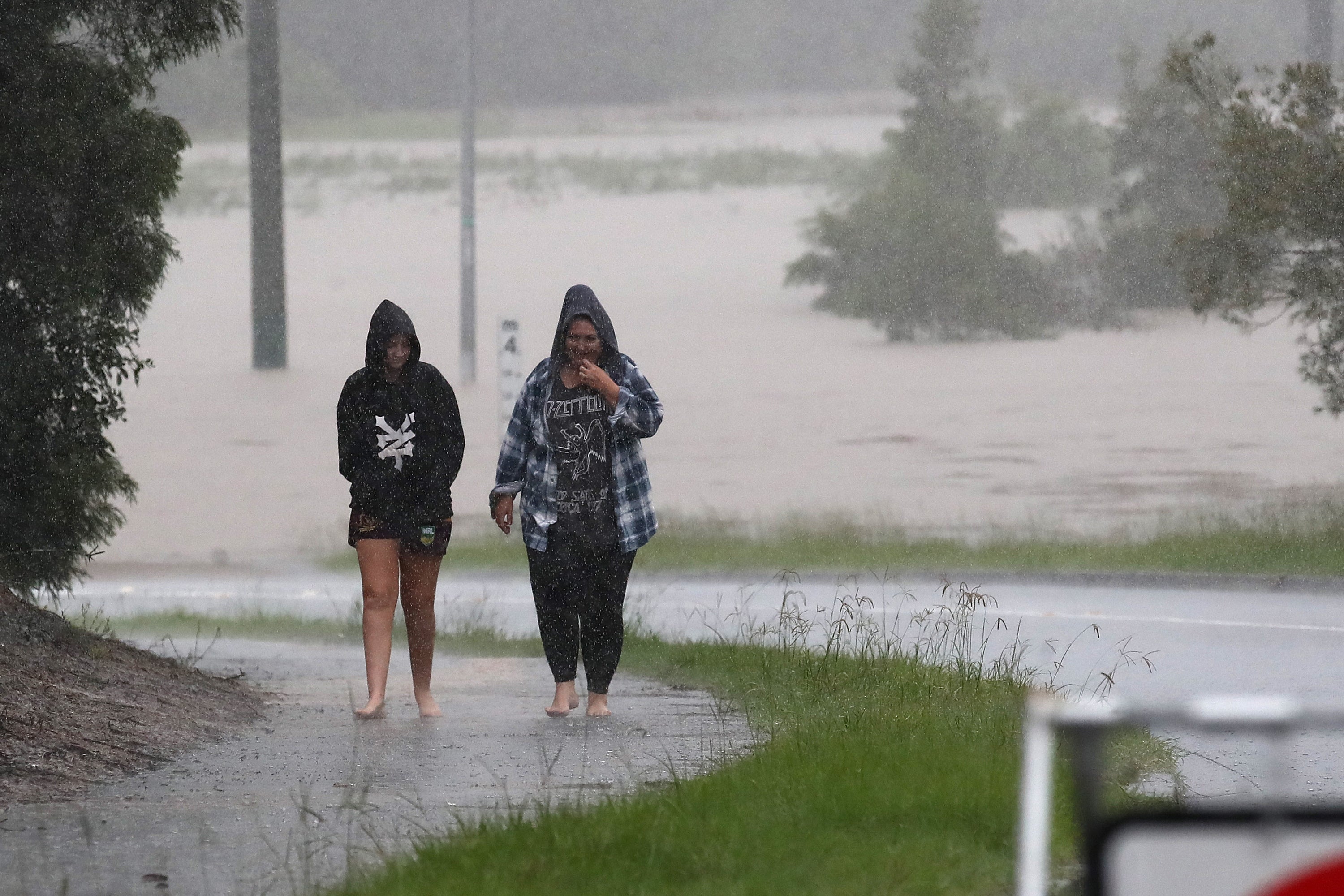 People walk in rain near a flooded road in Logan, southeast Queensland