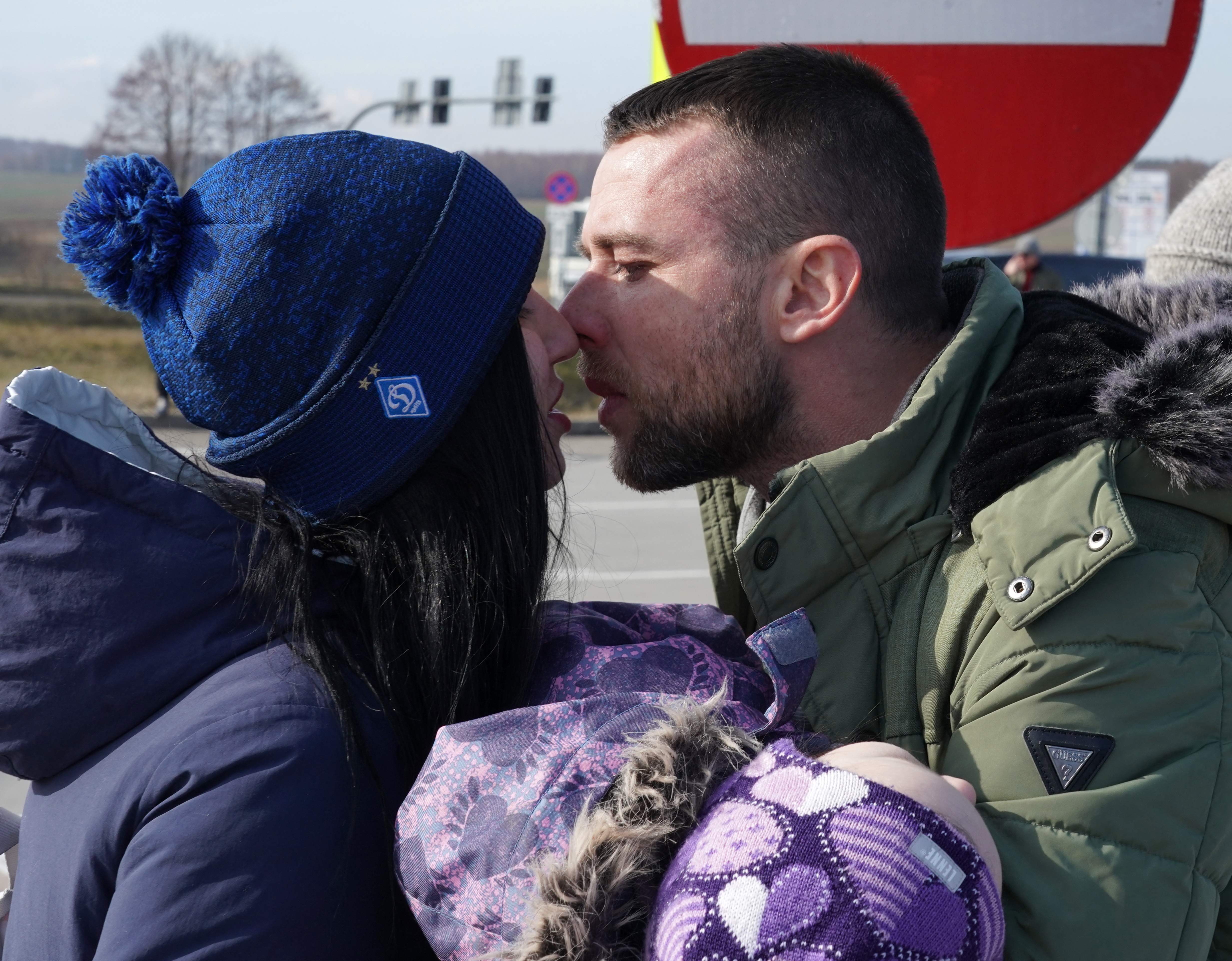 A Ukrainian man with a child kisses his wife as Ukrainians cross the border from Ukraine to Poland