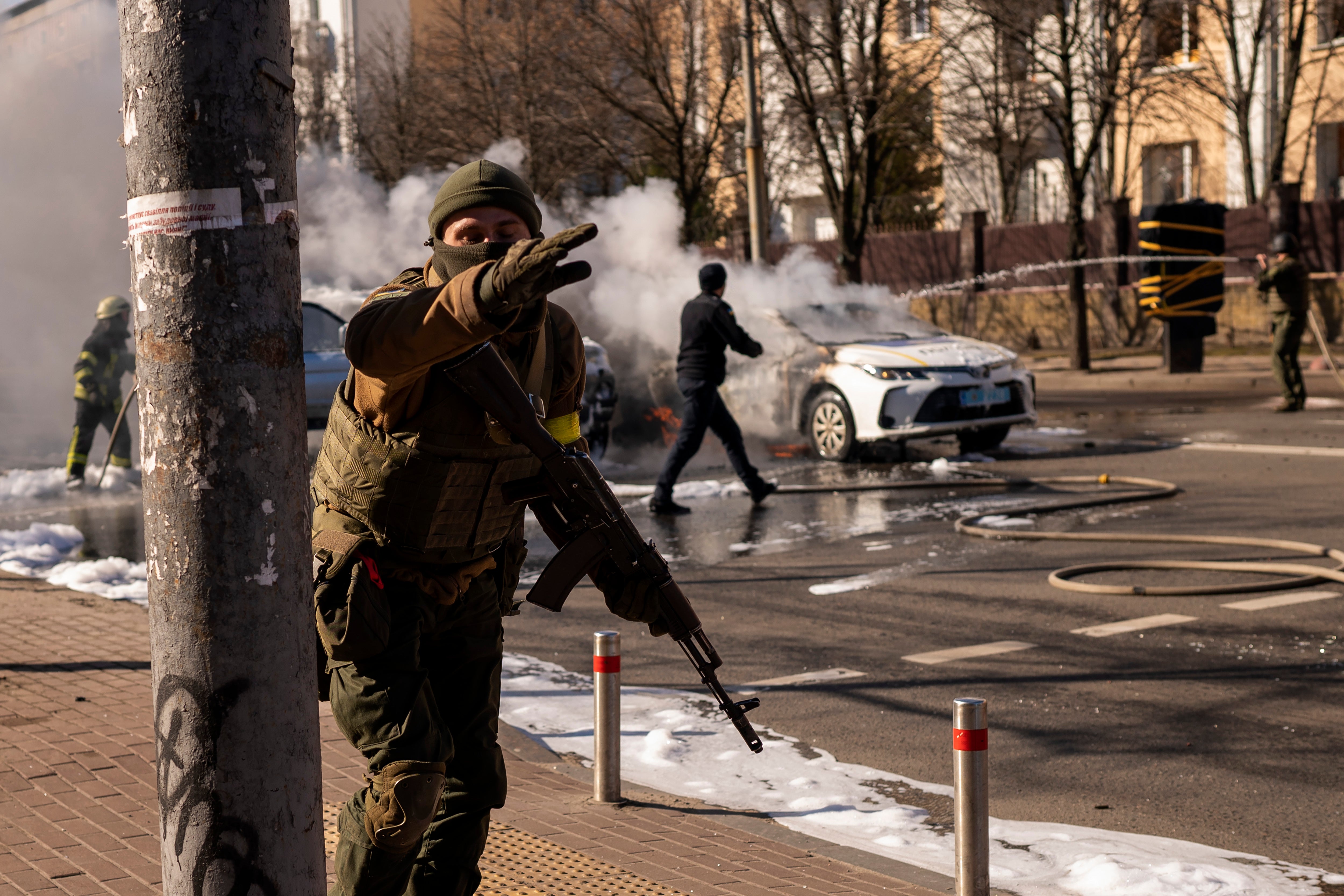 Ukrainian soldiers take positions outside a military facility as two cars burn, in a street in Kyiv