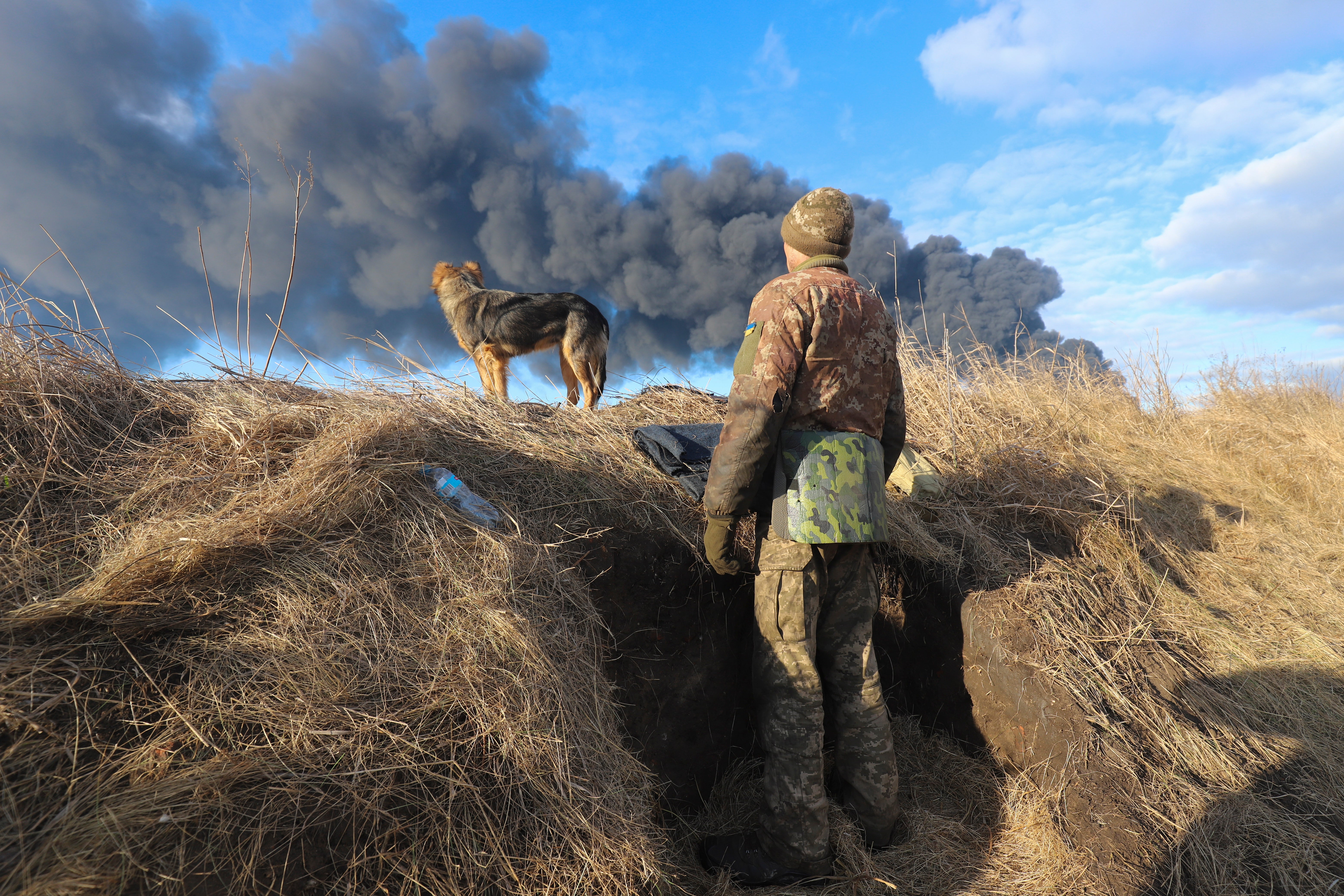 A Ukrainian serviceman and his dog stands in a position looking at smoke from a burned petroleum storage depot in Kharkiv