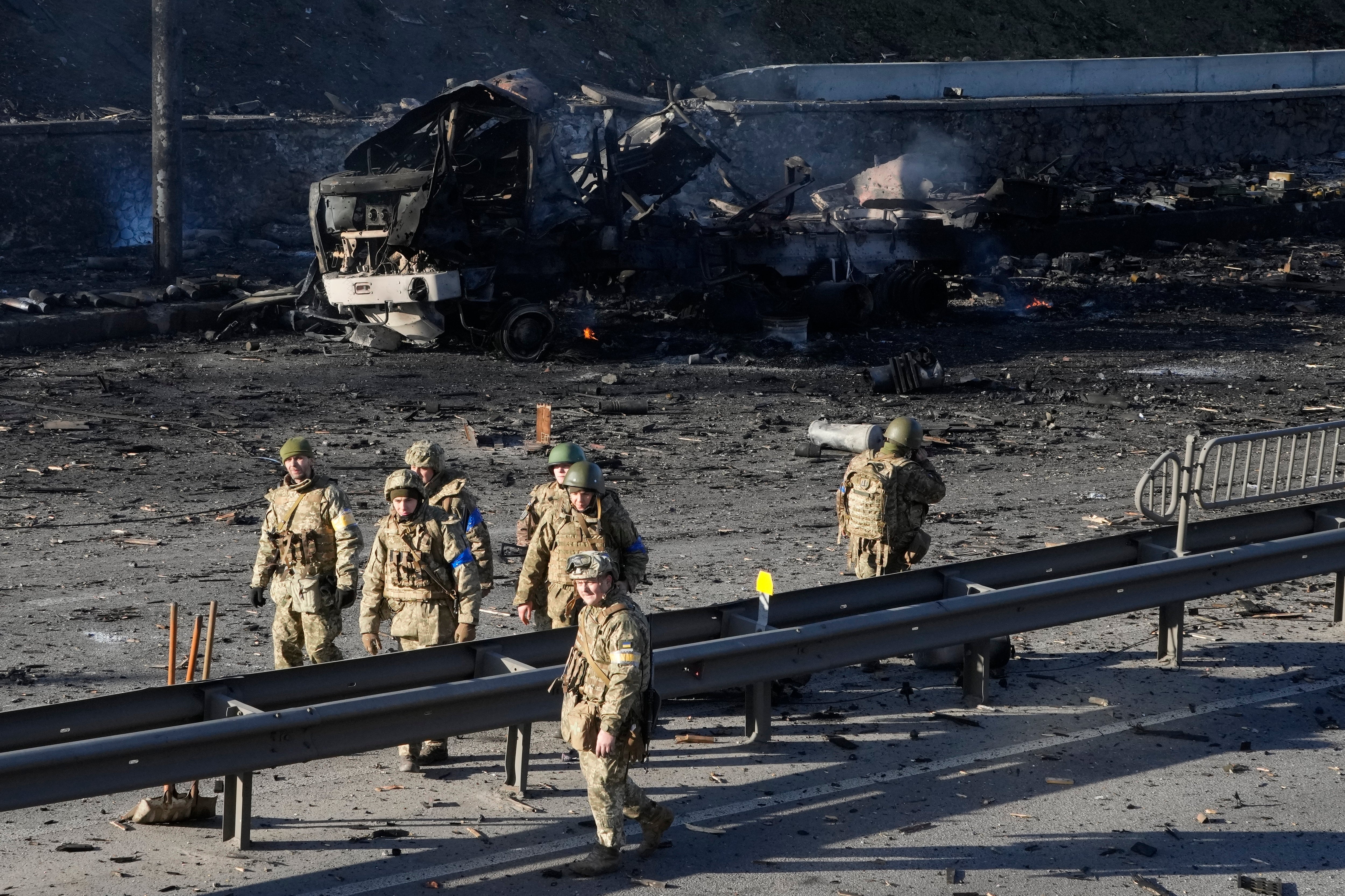 Ukrainian soldiers walk past debris of a burning military truck on a street in Kyiv, Ukraine, Saturday, Feb. 26, 2022