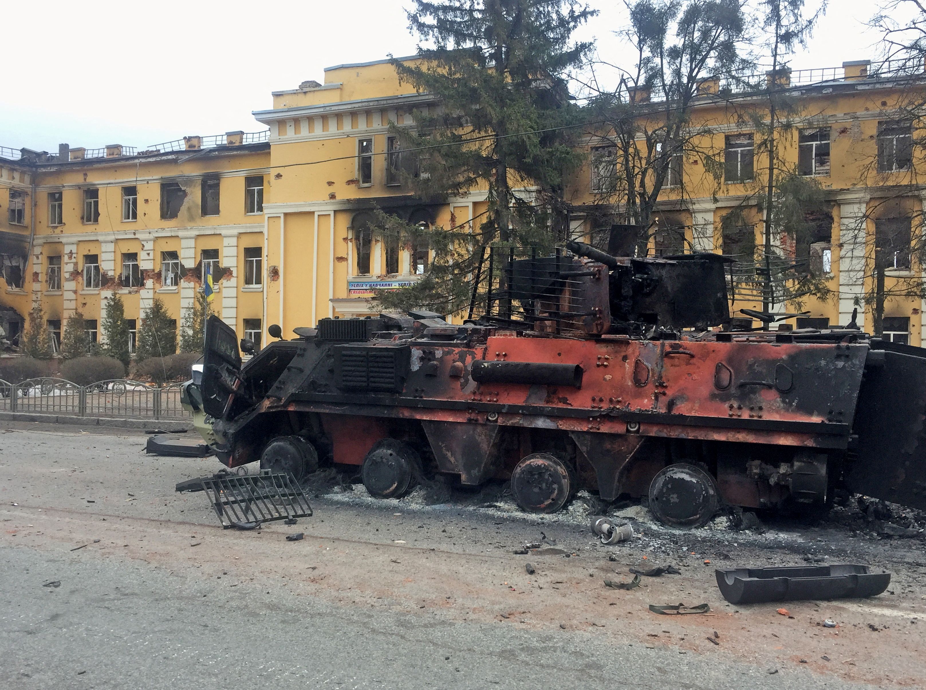 A destroyed Ukrainian armoured personnel carrier vehicle is seen in front of a school which, according to local residents, was on fire after shelling