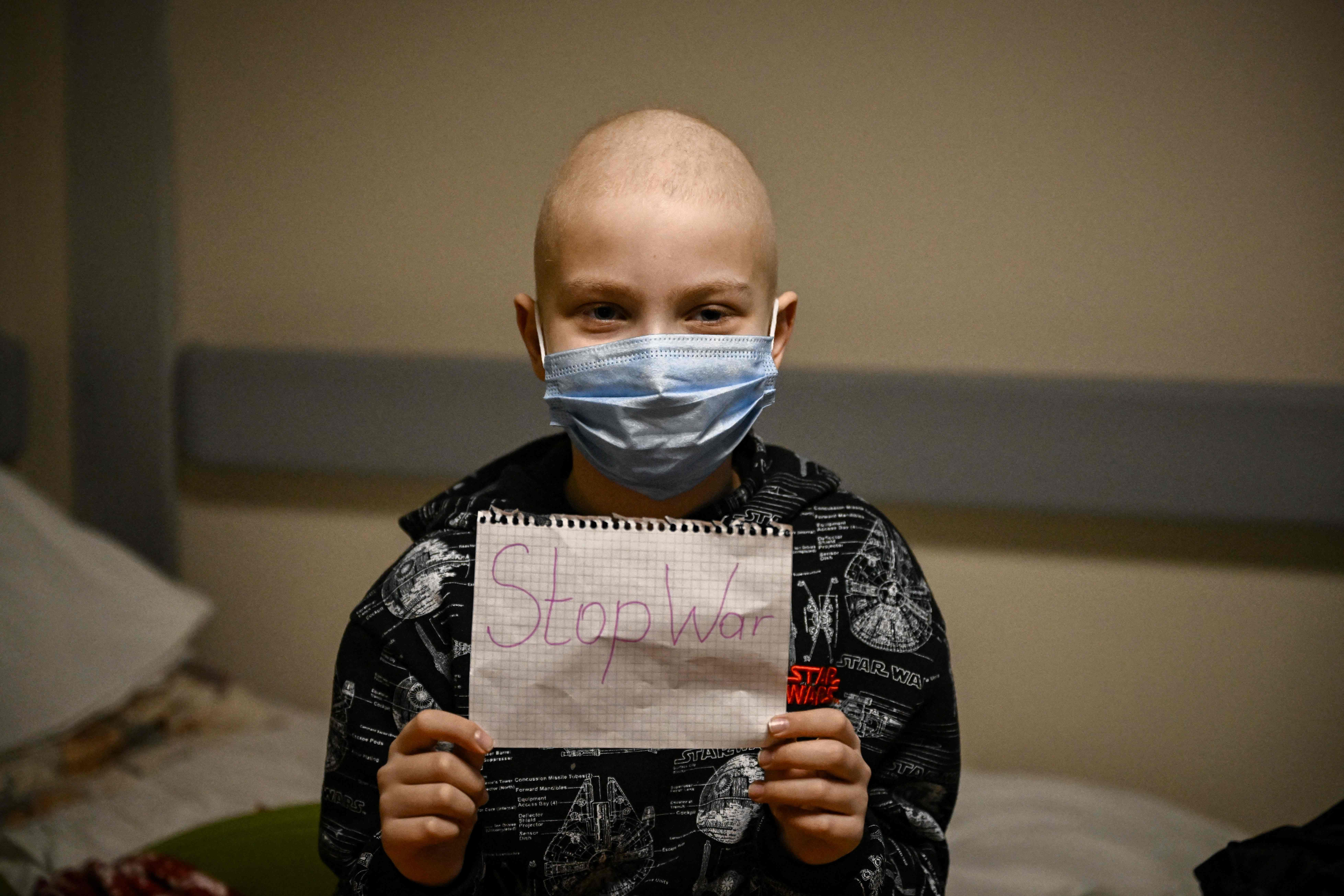 A child suffering from cancer holds a sign that says “Stop War” in the bomb shelter of an oncology centre in Kyiv