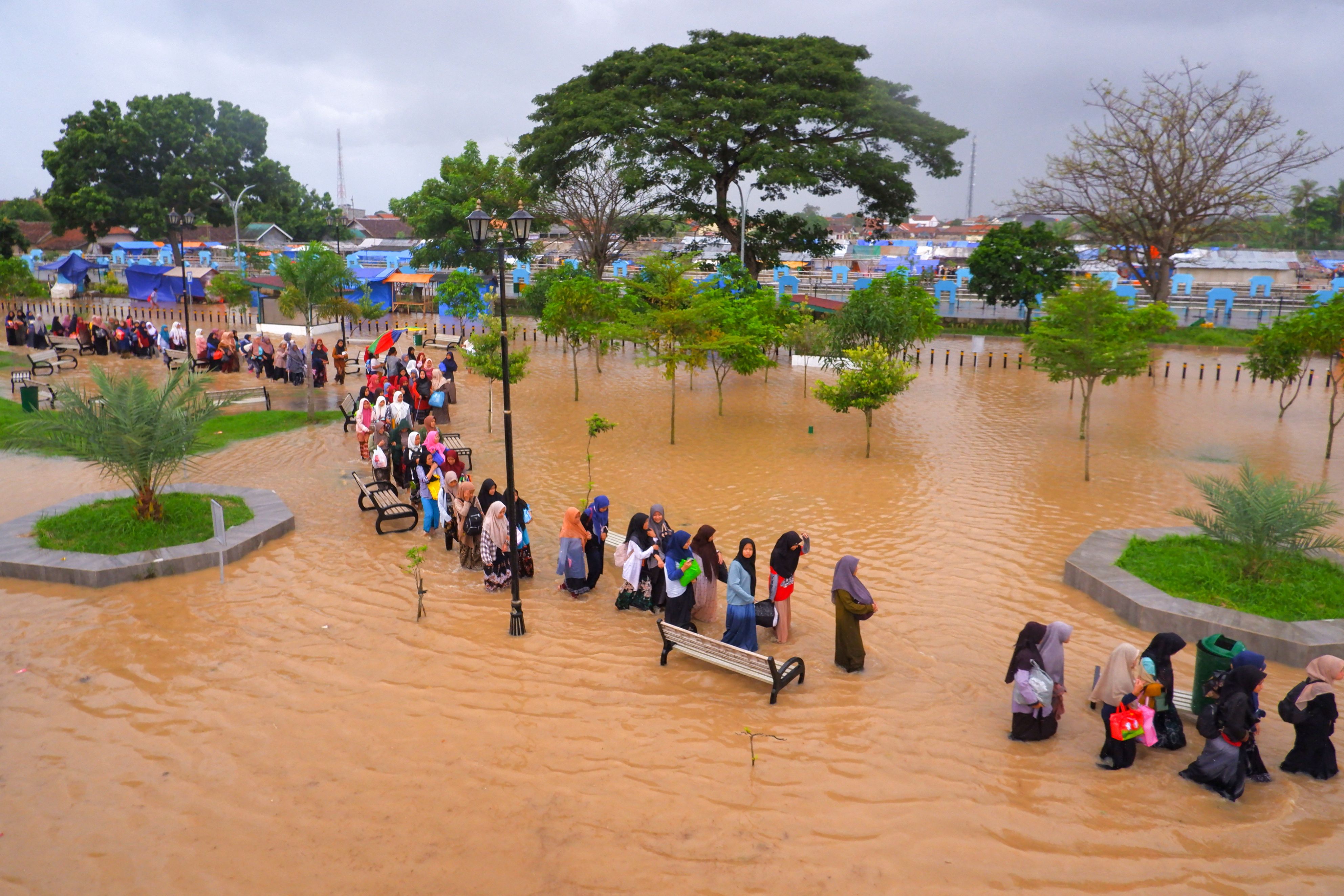 People wade floodwaters as they evacuate after floods in Serang, Banten province on March 1, 2022