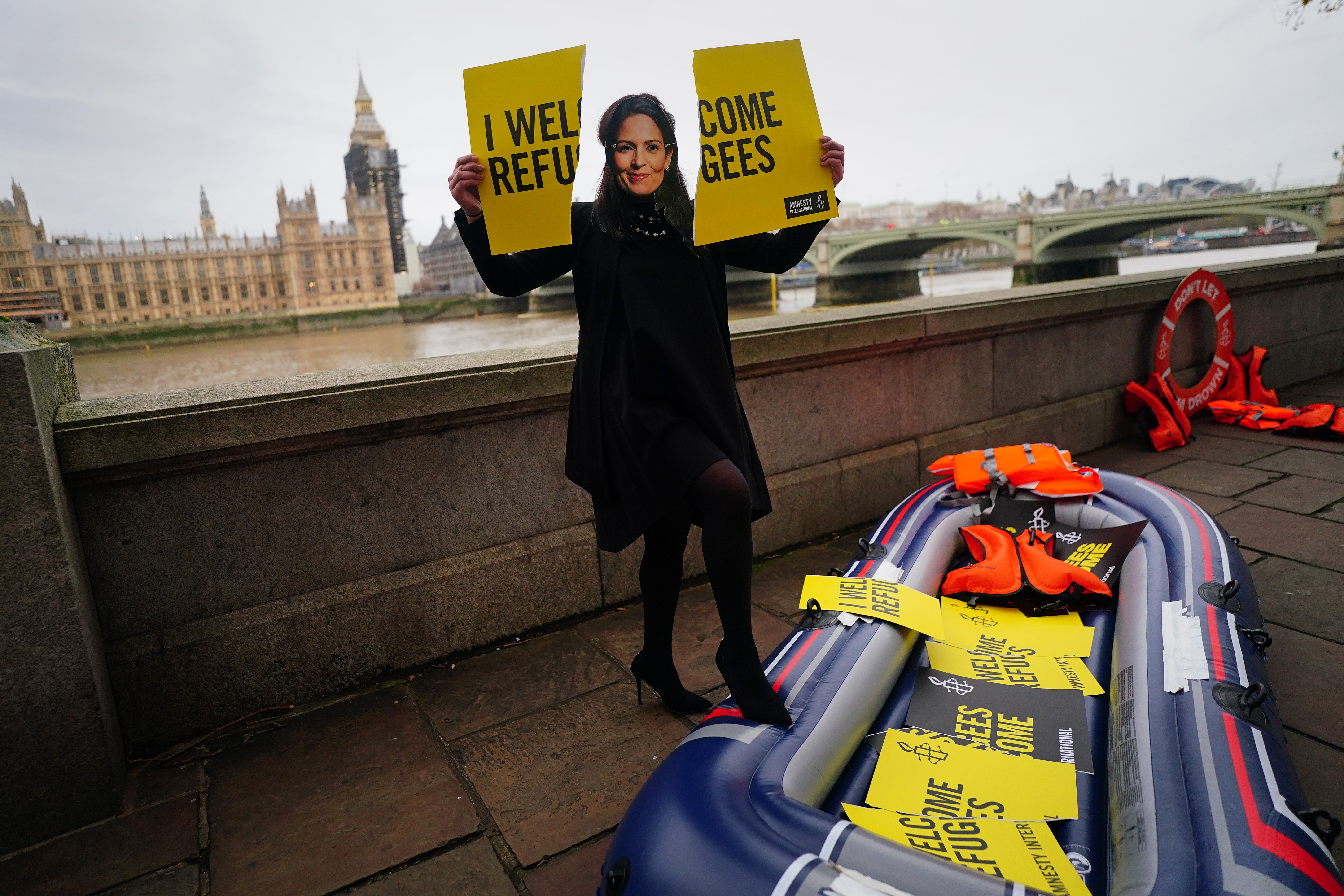 An Amnesty International campaigner wearing a Priti Patel mask tears up a 'Refugees Welcome'