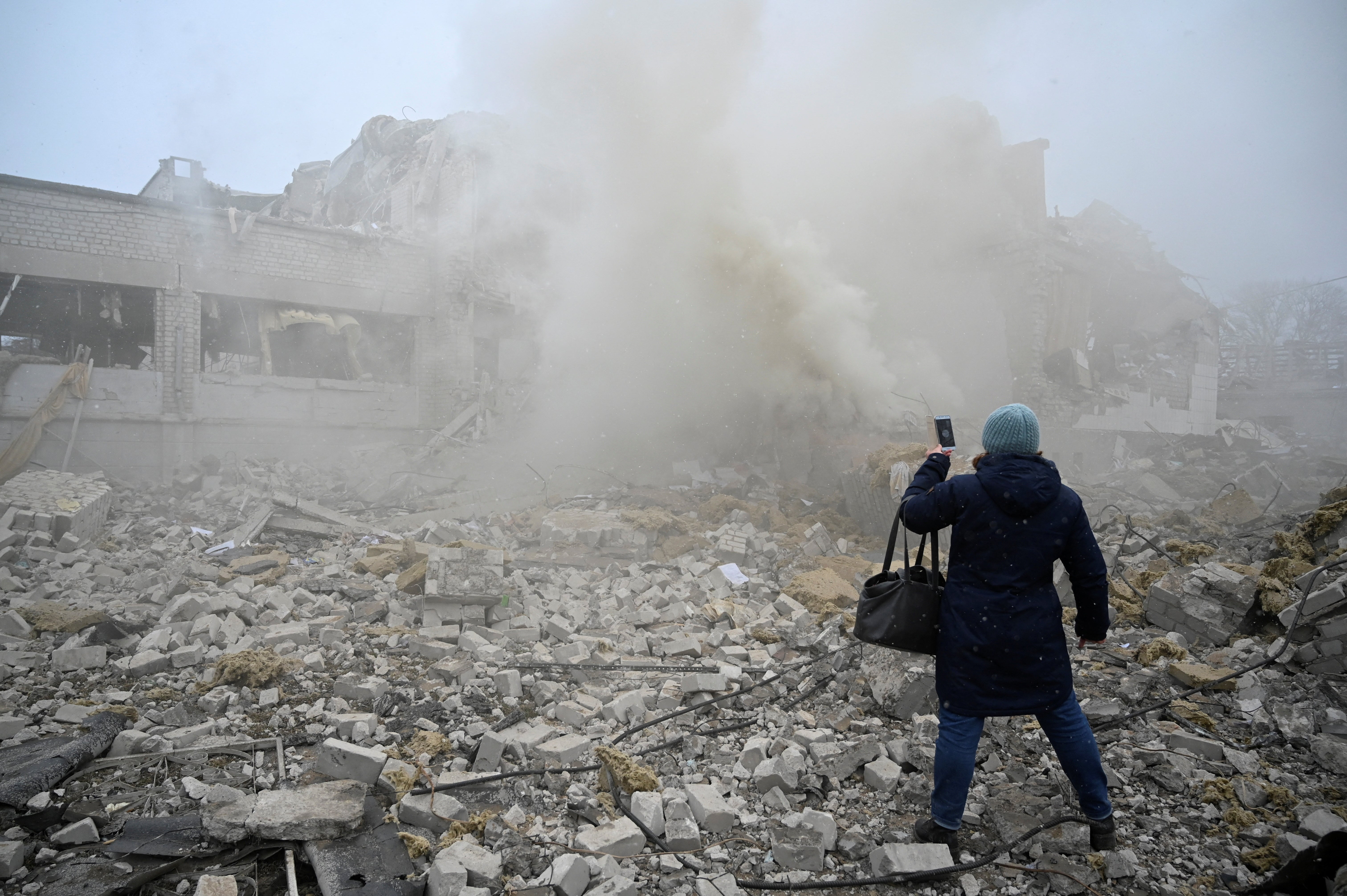 A woman uses a mobile phone while standing amidst the debris of the school building in Zhytomyr