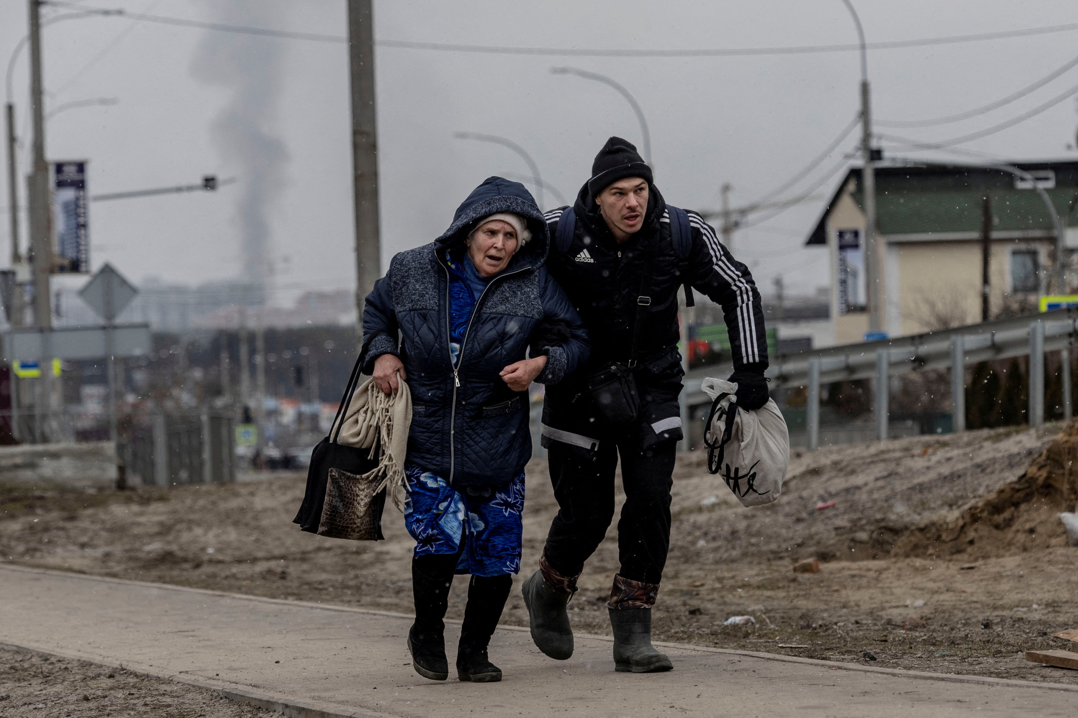 A man helps an elderly woman to run for cover after heavy shelling on the only escape route used by locals, while Russian troops advance towards the capital, in Irpin, near Kyiv, 6 March 2022