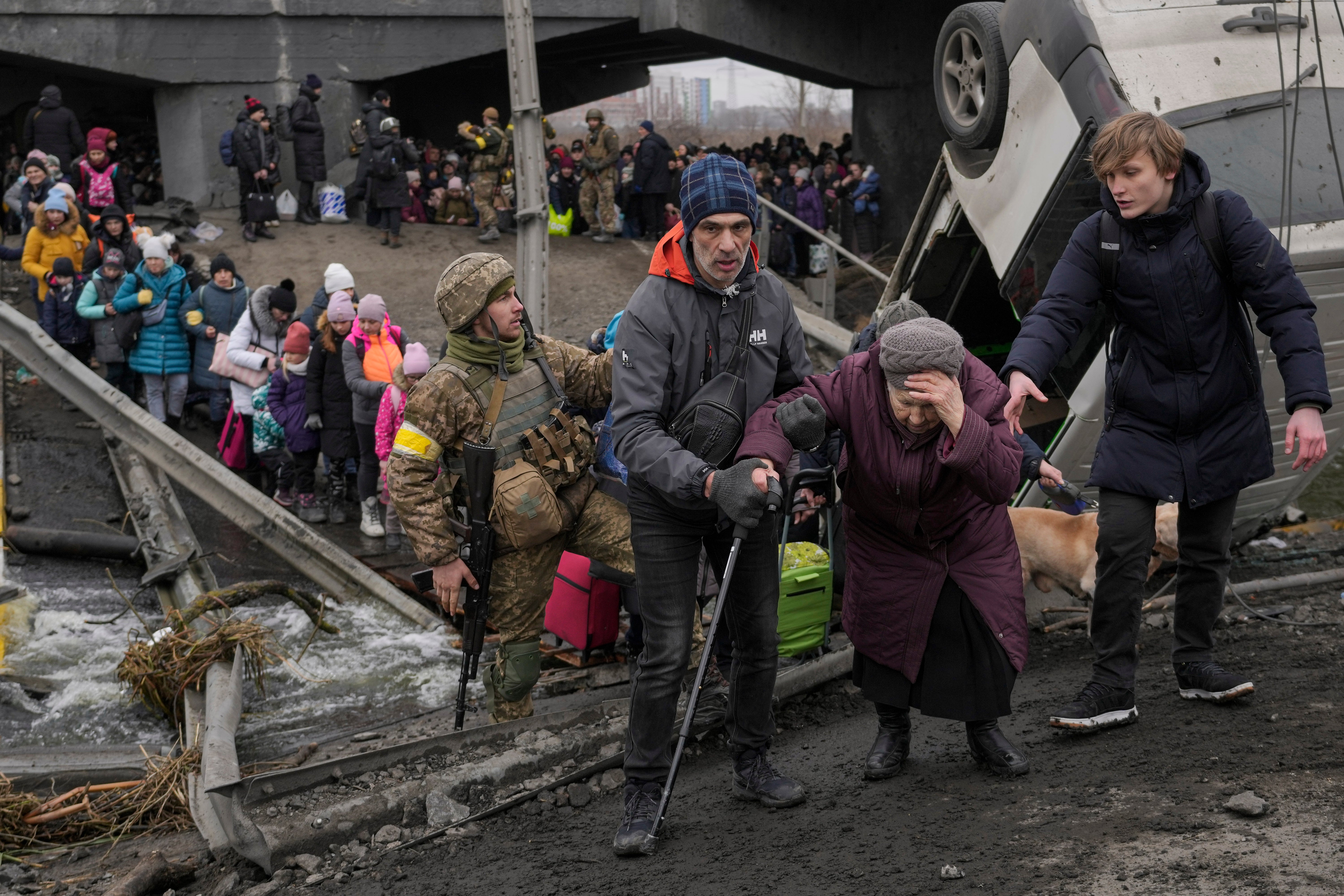 An elderly lady is assisted while crossing the Irpin river, under a bridge that was destroyed by a Russian airstrike