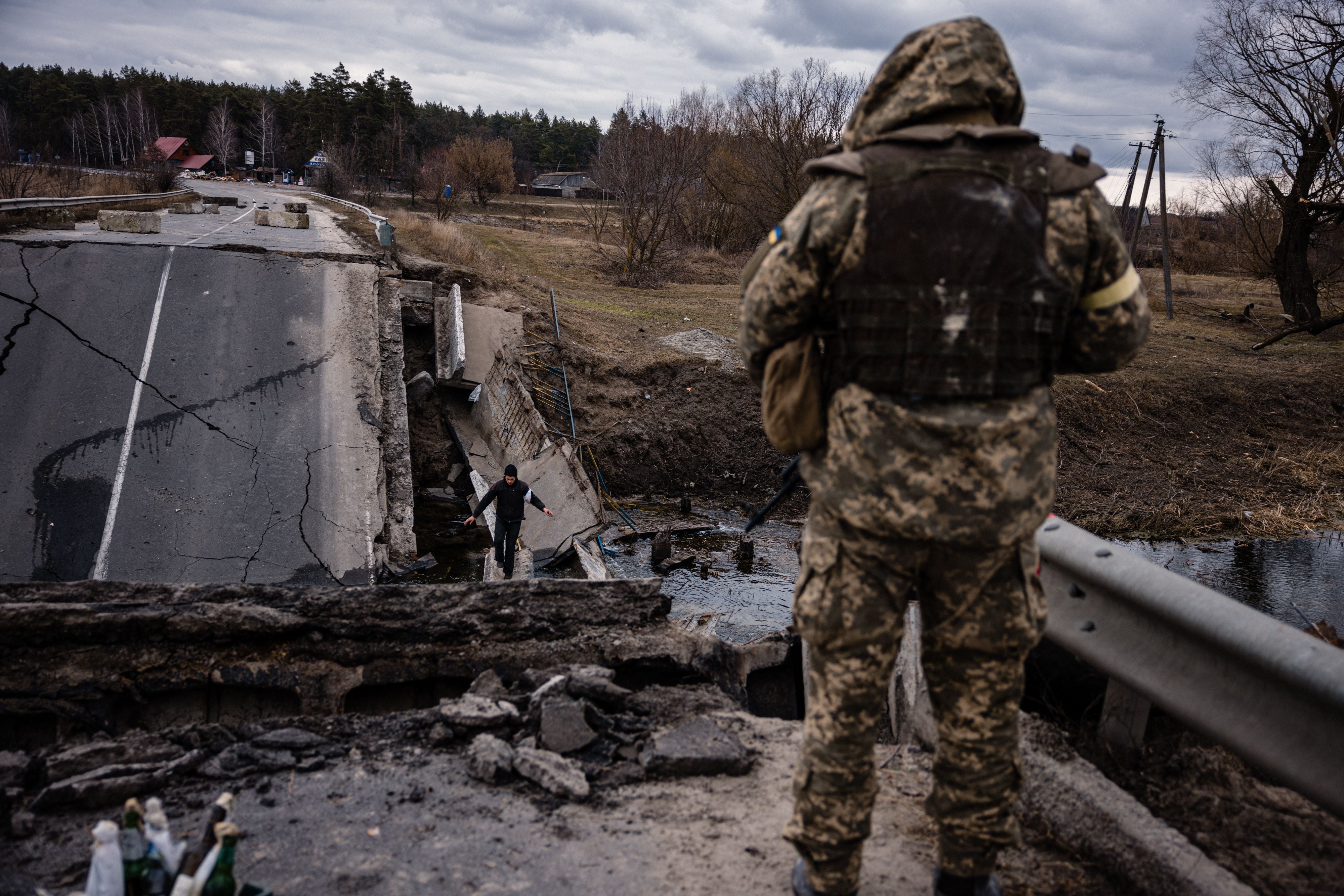 A Ukrainian serviceman looks at a civilian crossing a destroyed bridge in a village, east of the town of Brovary near Kyiv on Sunday