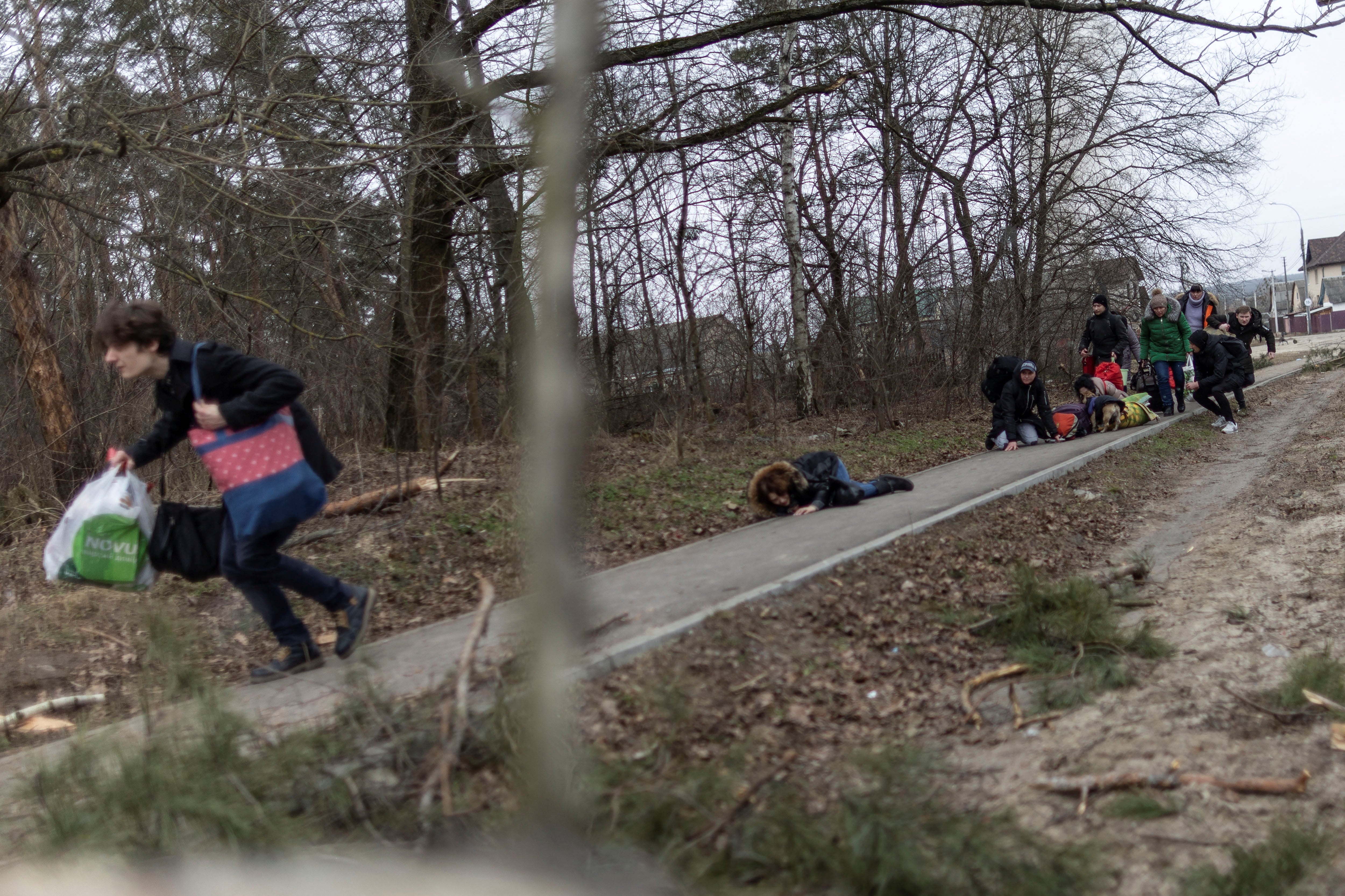 Local residents look for cover as they escape from the town of Irpin.