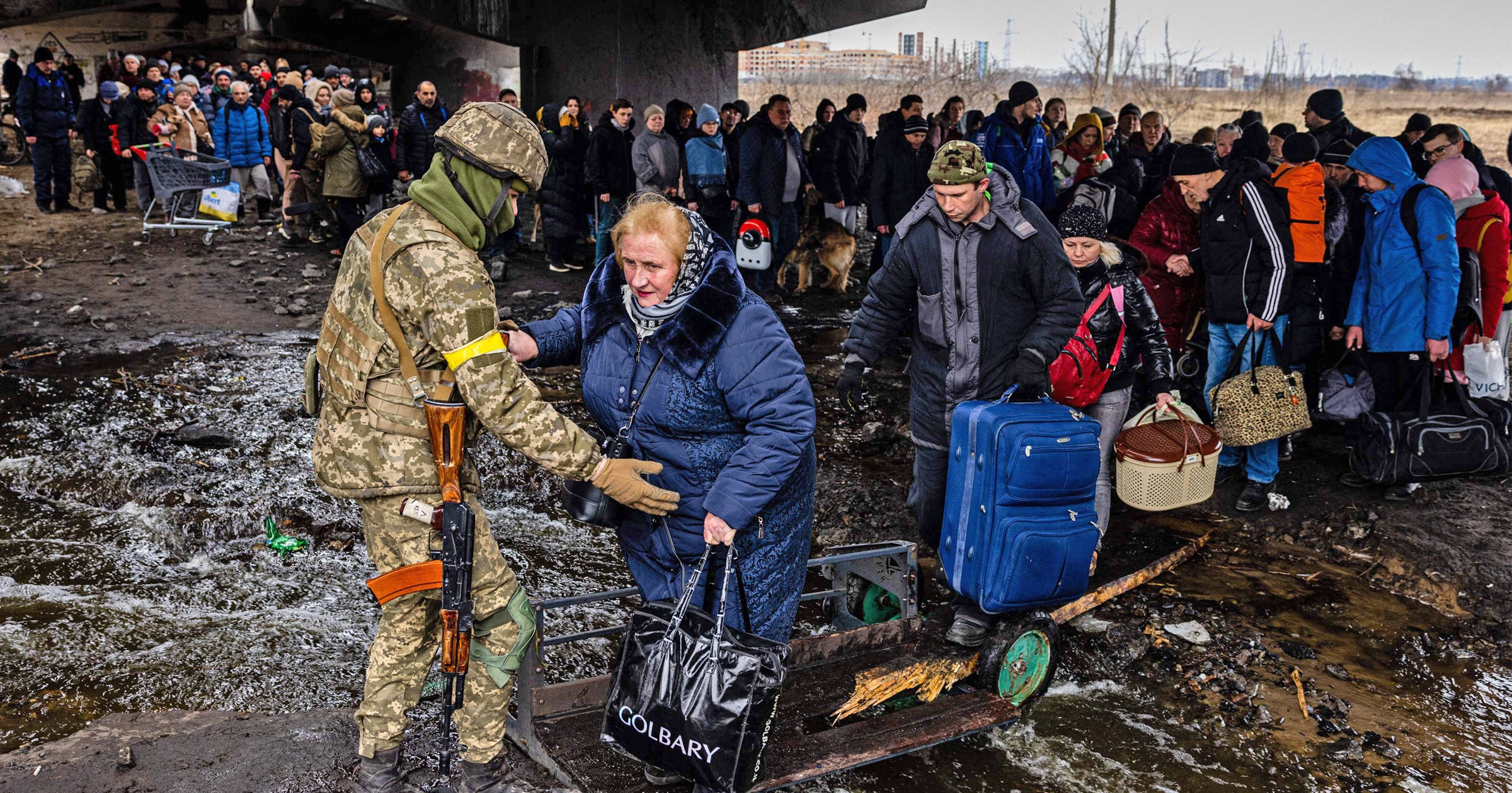 A Ukrainian serviceman helps evacuees gathered under a destroyed bridge, as they flee the city of Irpin, northwest of Kyiv, on 7 March