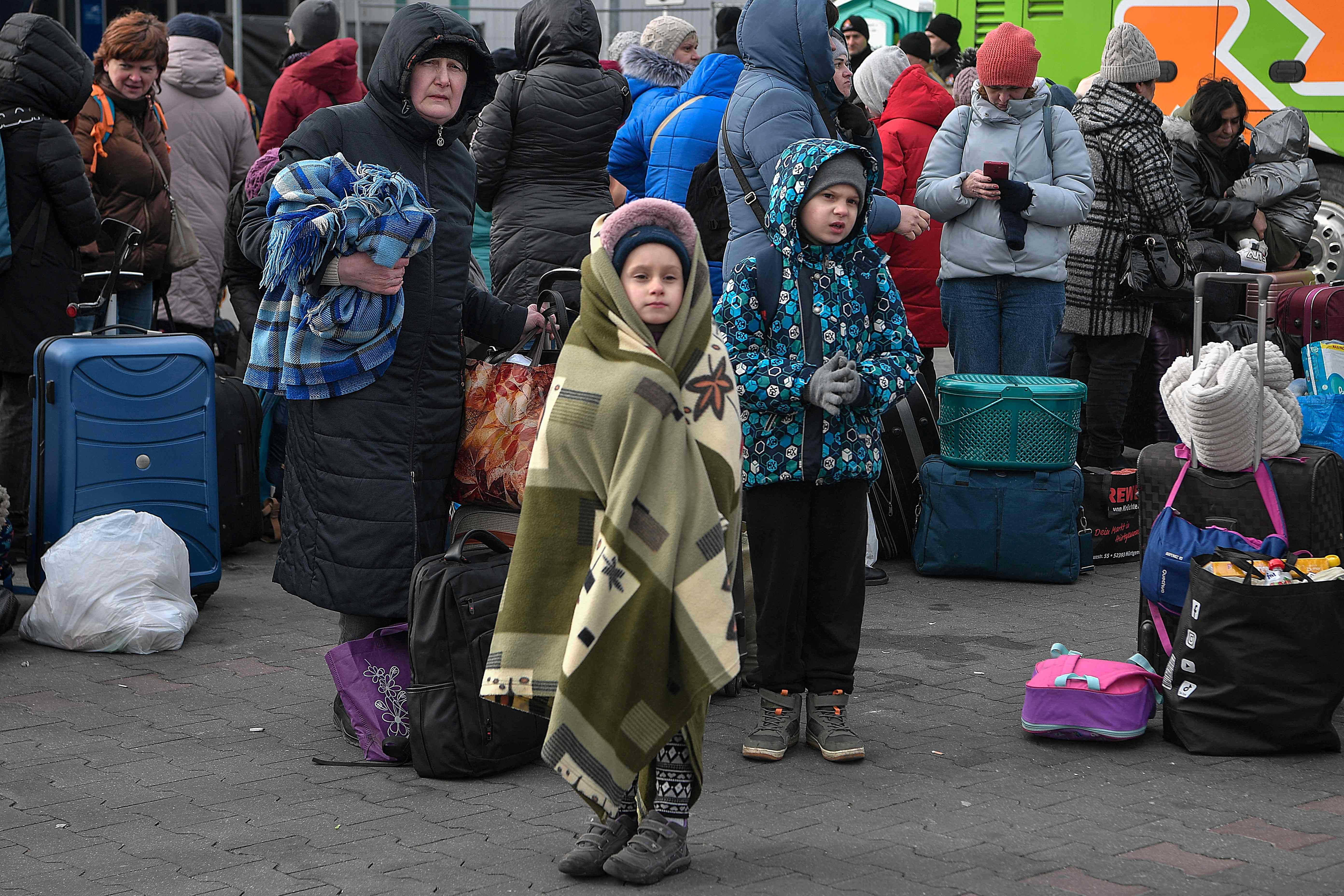 People stand with their luggage as they wait to board buses transporting them further into Poland or abroad from the temporary shelter for refugees located in a former shopping centre between the Ukrainian border and the Polish city of Przemysl