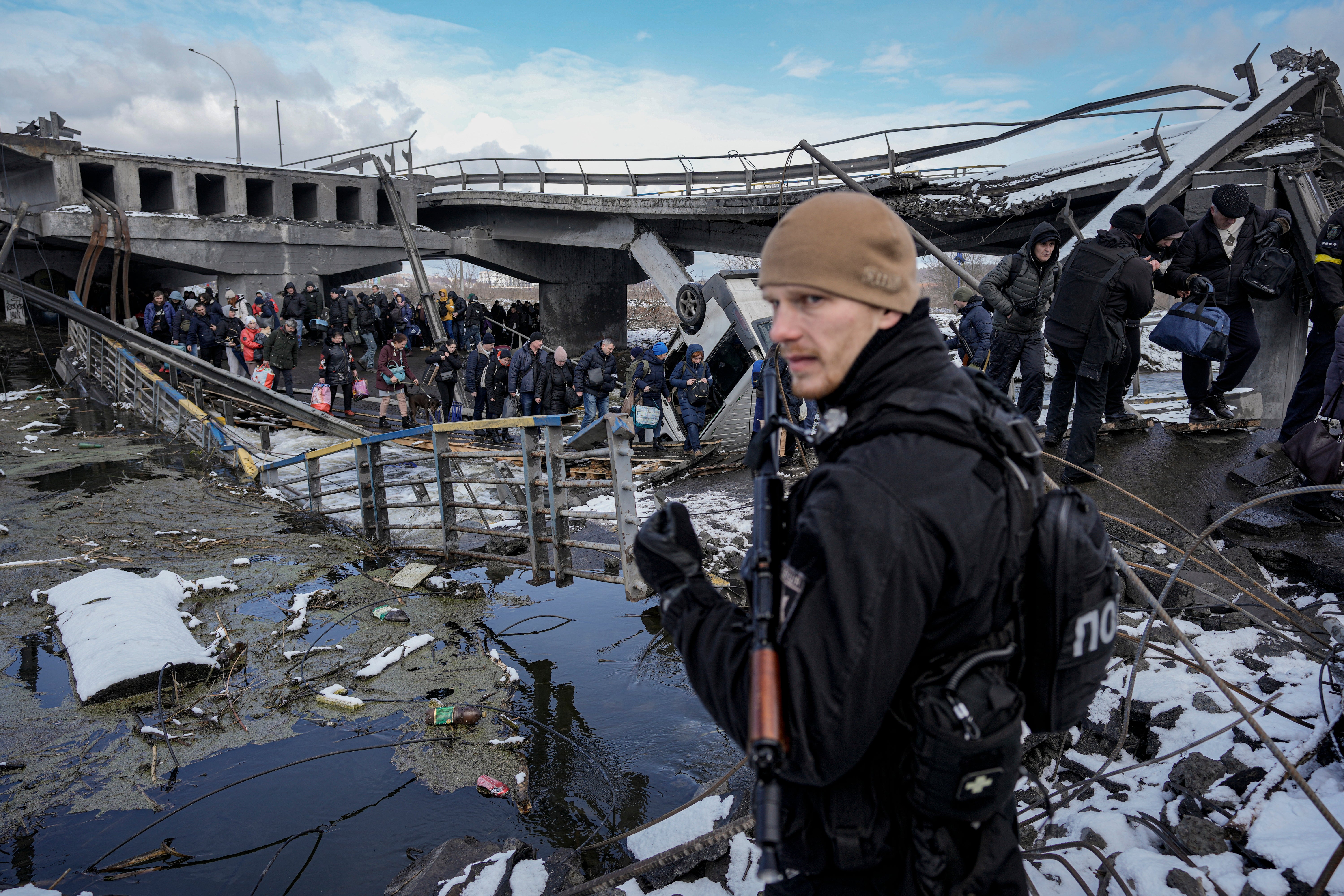 People walk under a destroyed bridge while fleeing Irpin, on the outskirts of Kyiv