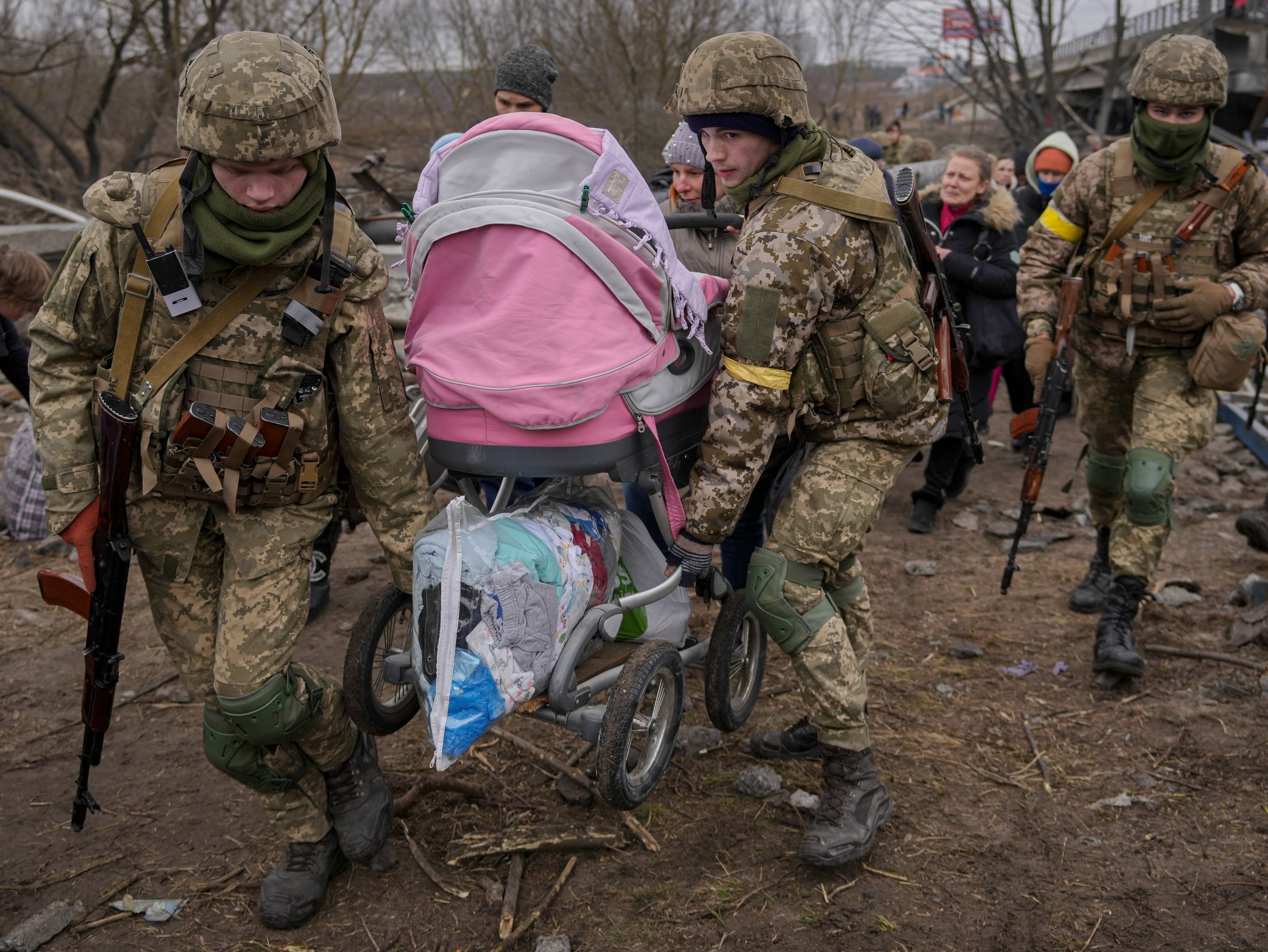 Ukrainian servicemen carry a baby stroller after crossing the Irpin river on an improvised path under a bridge, that was destroyed by Ukrainian troops designed to slow any Russian military advance