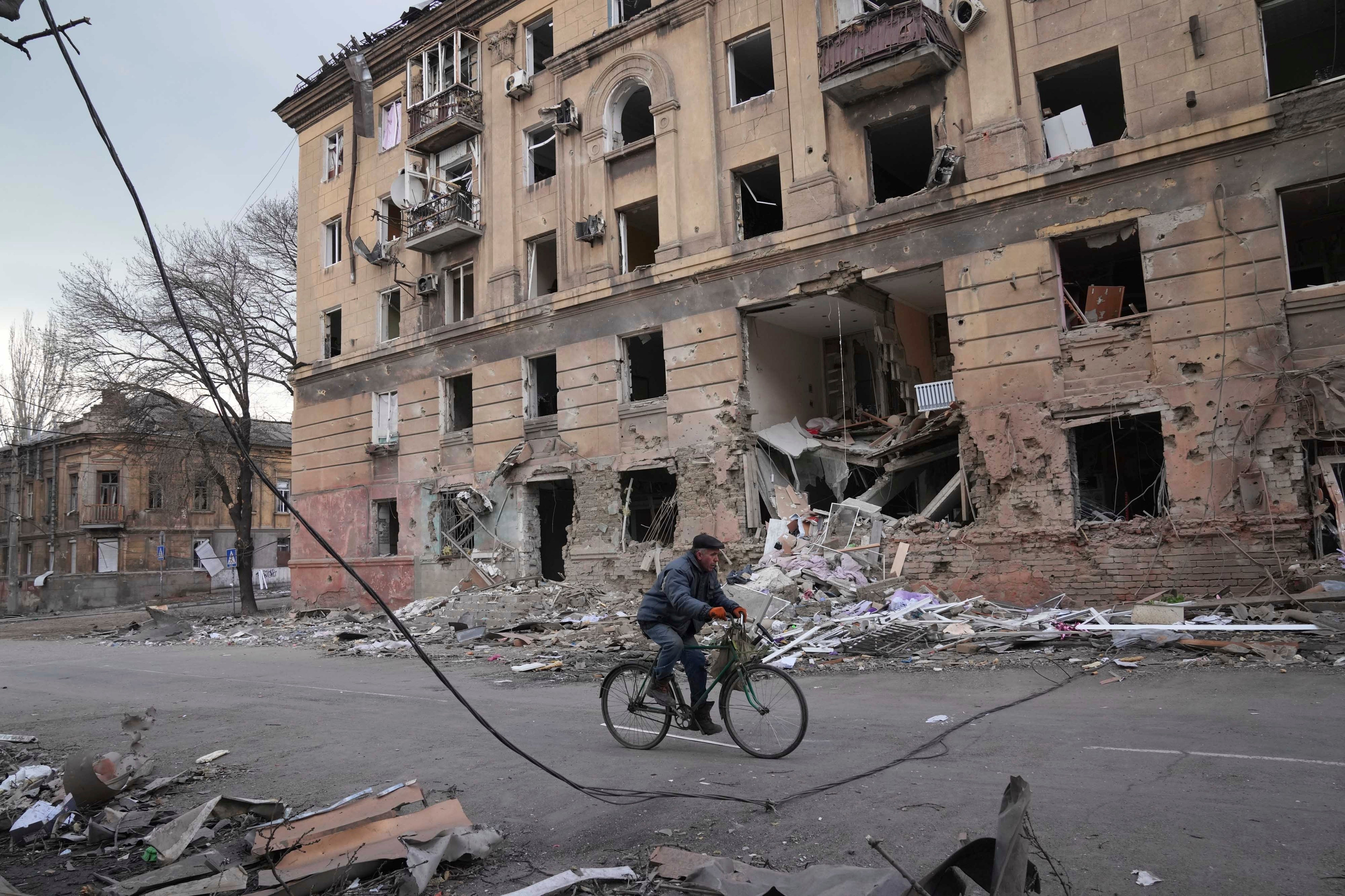 A man rides a bicycle in front of a damaged by shelling apartment building in Mariupol, Ukraine, Wednesday, March 9, 2022.