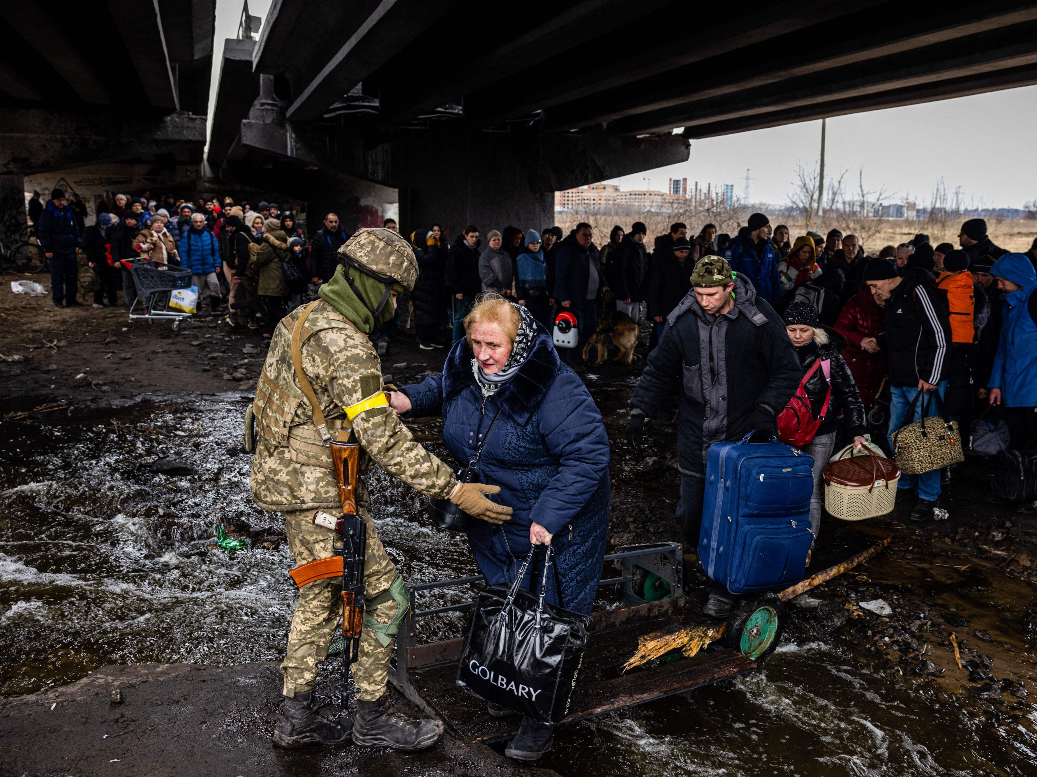 A Ukrainian serviceman helps evacuees gathered under a destroyed bridge, as they flee the city of Irpin