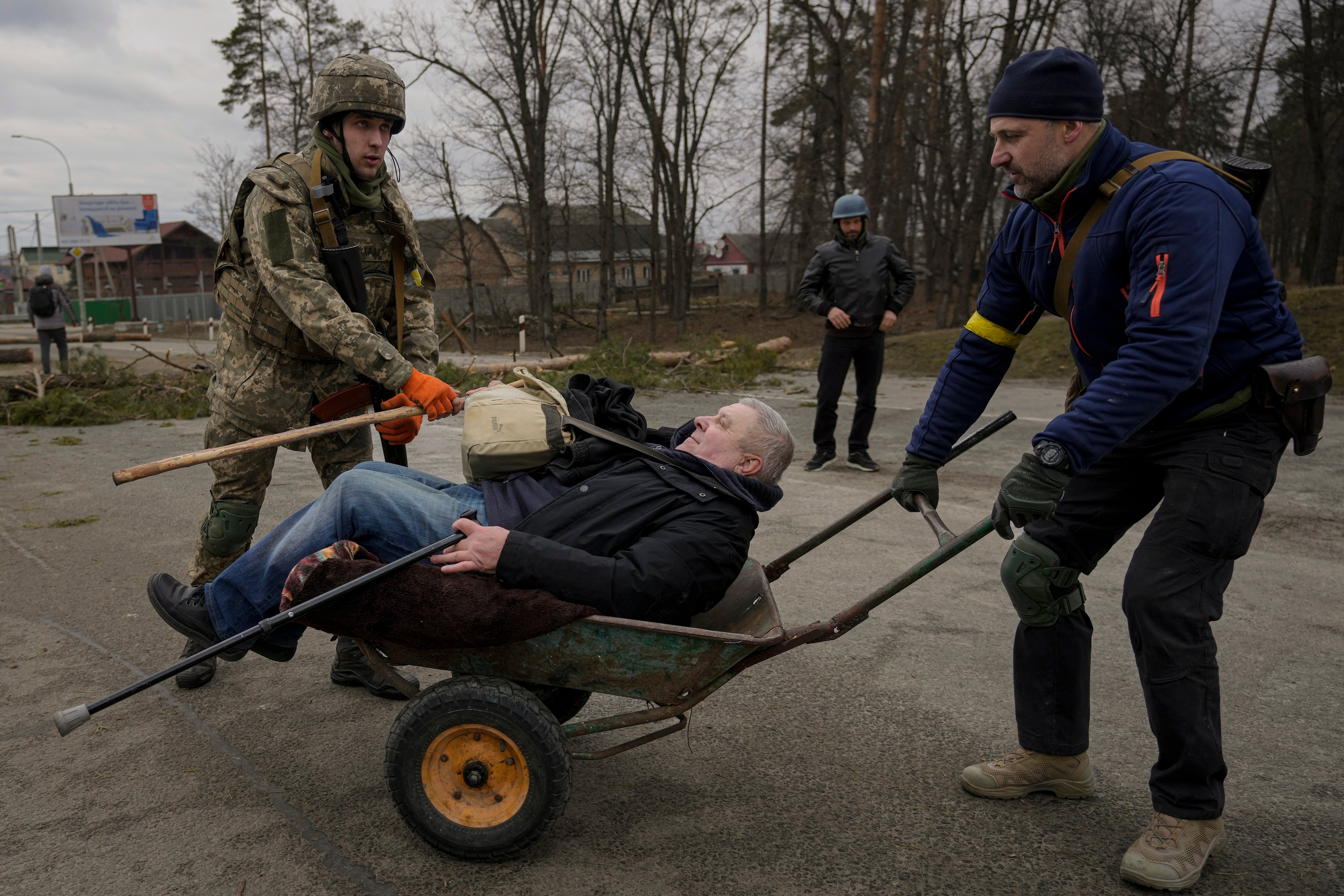 A man is helped in a wheelbarrow after crossing Irpin river on an improvised path under a bridge that was destroyed by Ukrainian troops designed to slow any Russian military advance, while fleeing the town of Irpin