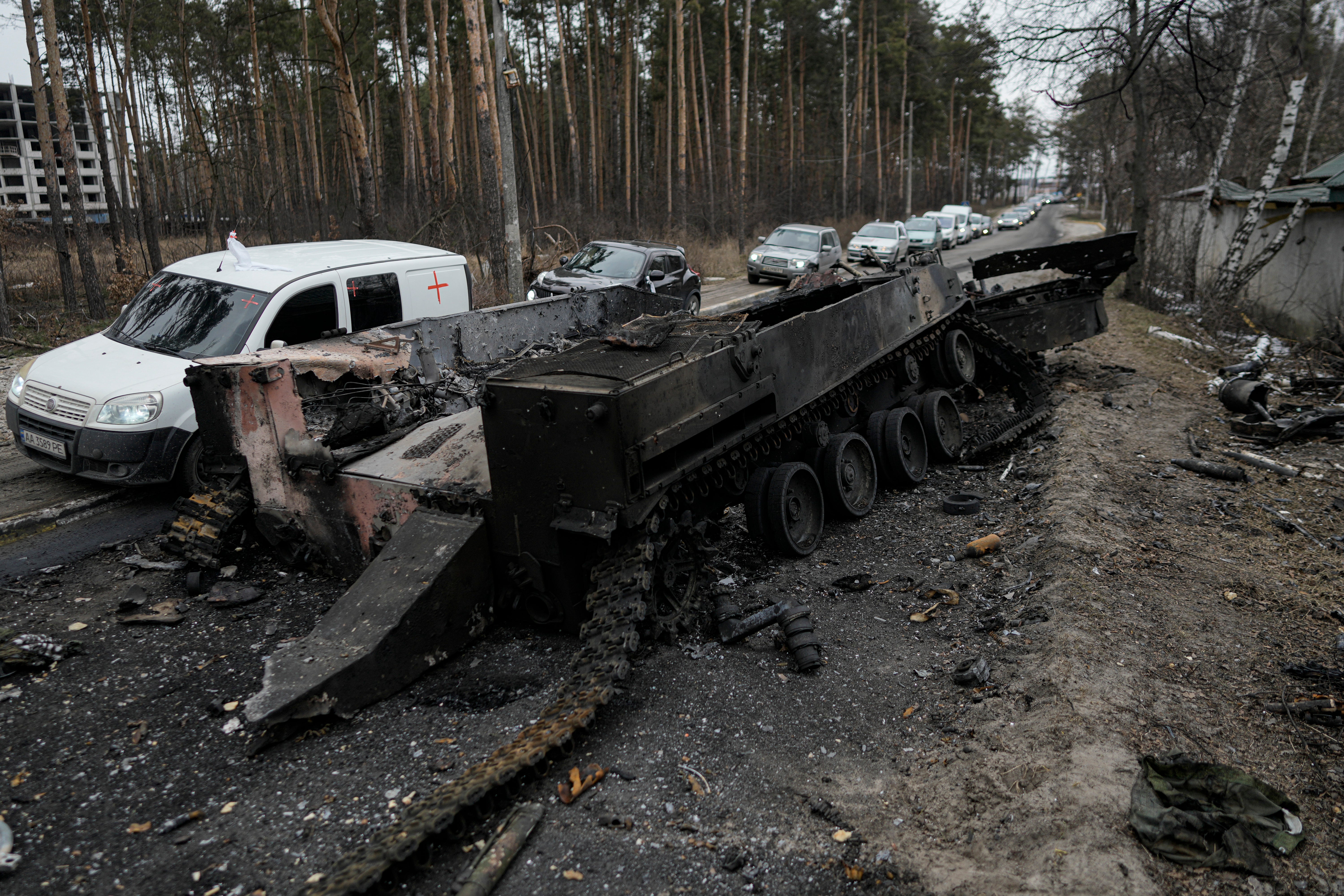 Cars drive past a destroyed Russian tank as a convoy of vehicles evacuating civilians leaves Irpin, on the outskirts of Kyiv, on 9 March