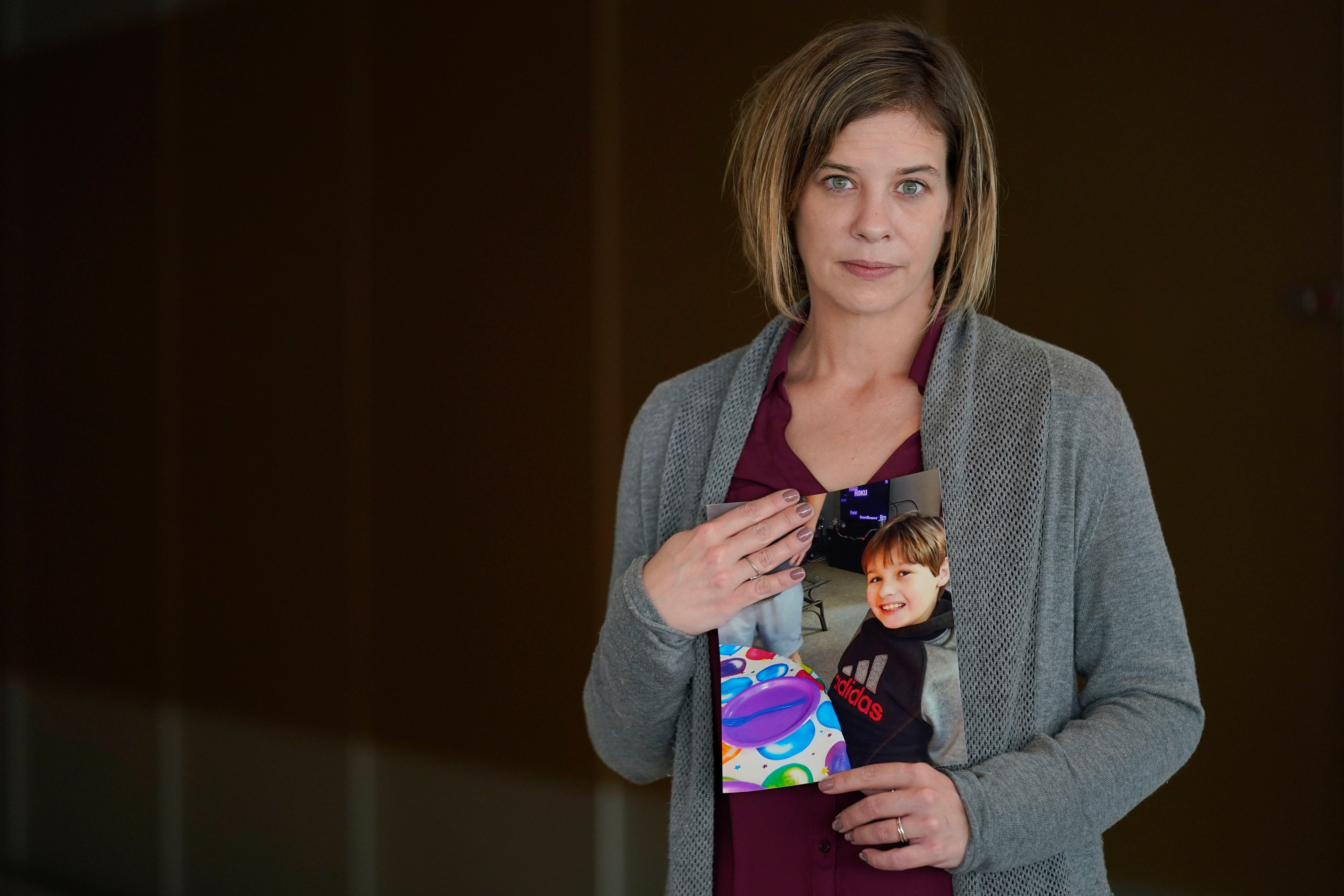 Kara Trainor poses for a picture with a photo of her son, Riley, 11, after making a statement during a hearing in New York, Thursday, March 10, 2022