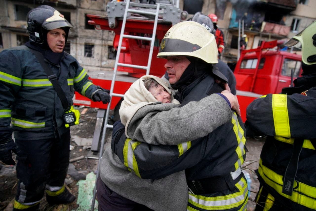 Rescuers help a woman evacuate a residential building that was struck