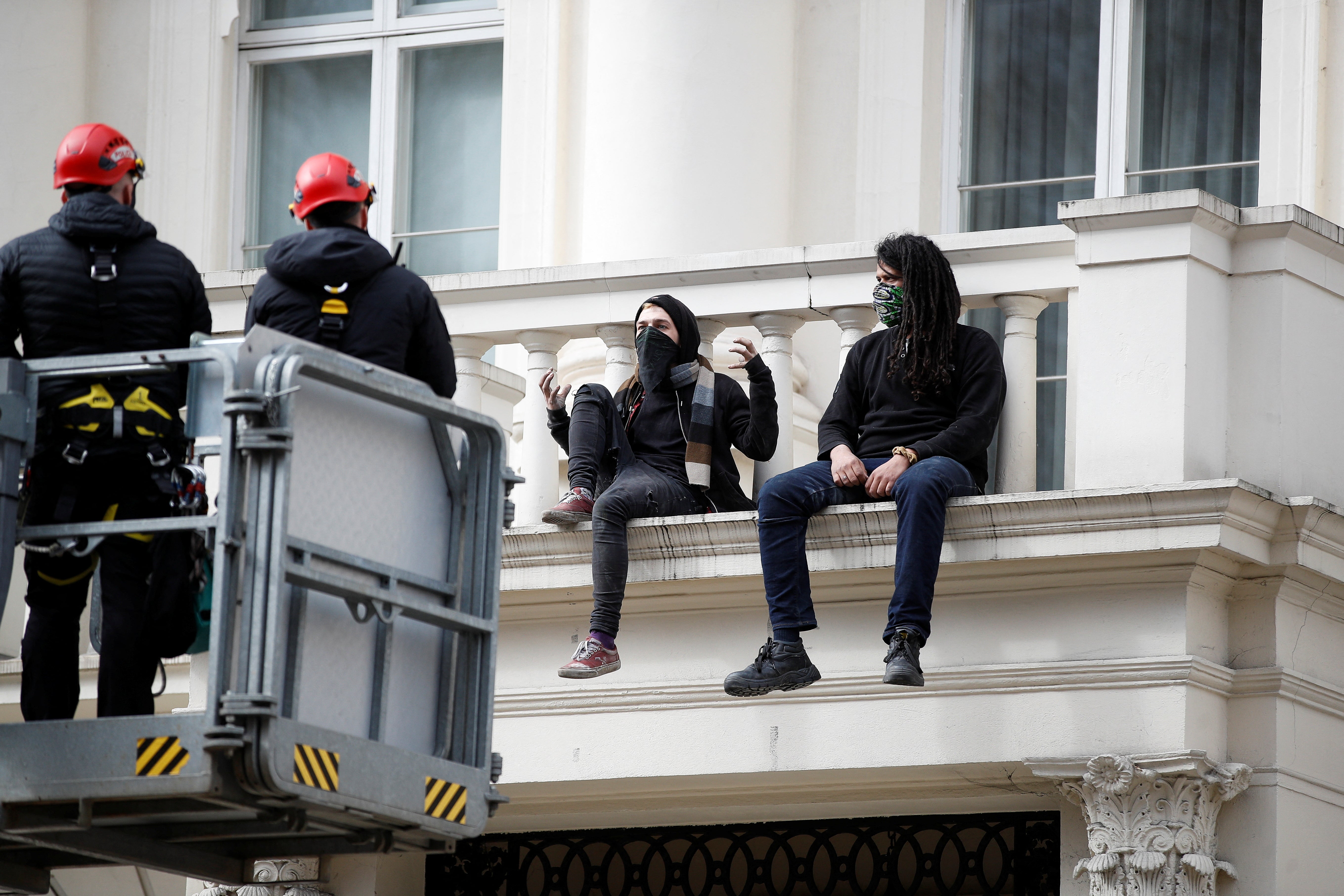 Police officers speak to squatters from a JCB cherry picker platform