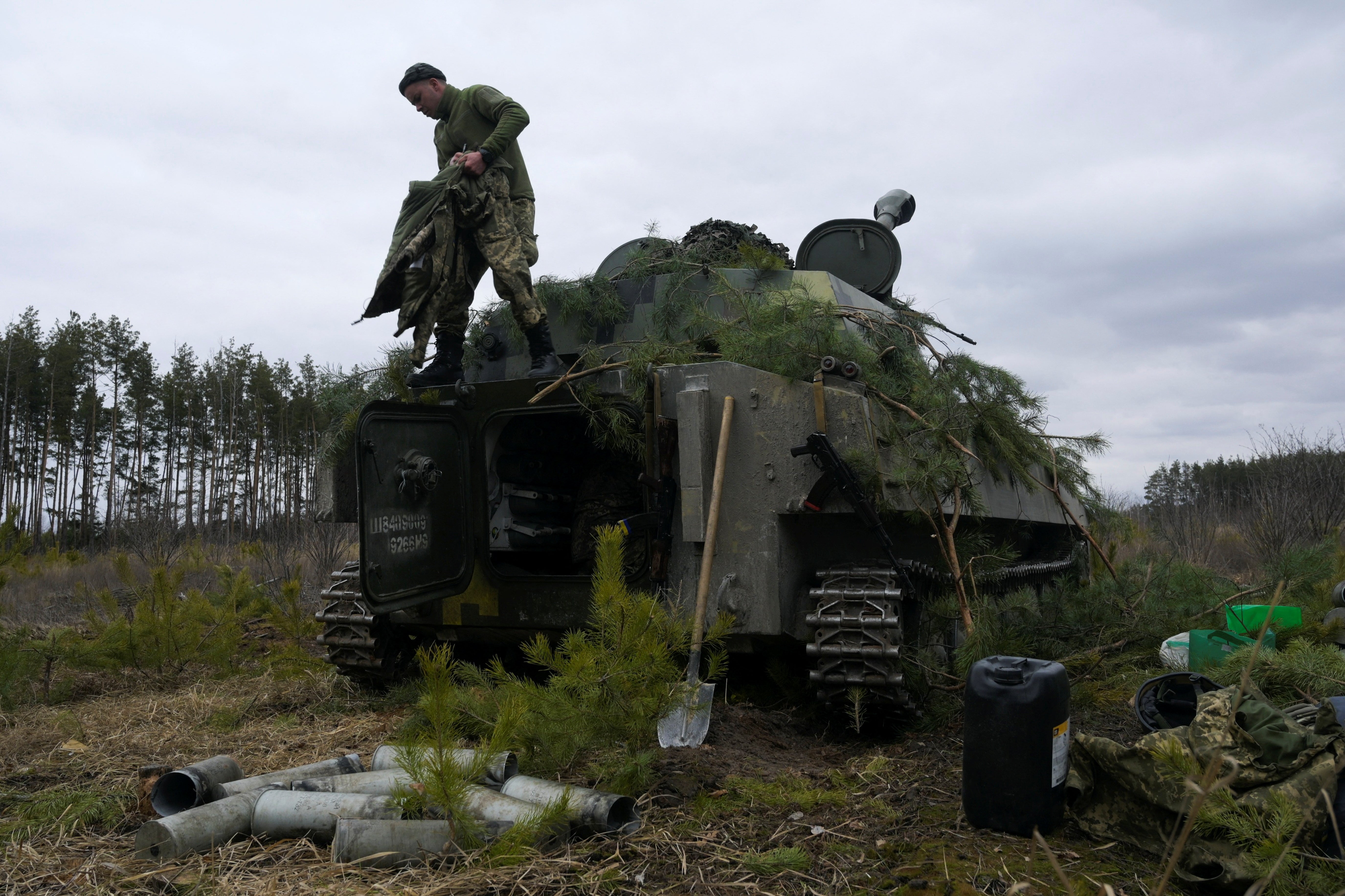 A service member of the Ukrainian armed forces conceals a self-propelled howitzer at a position near Makariv