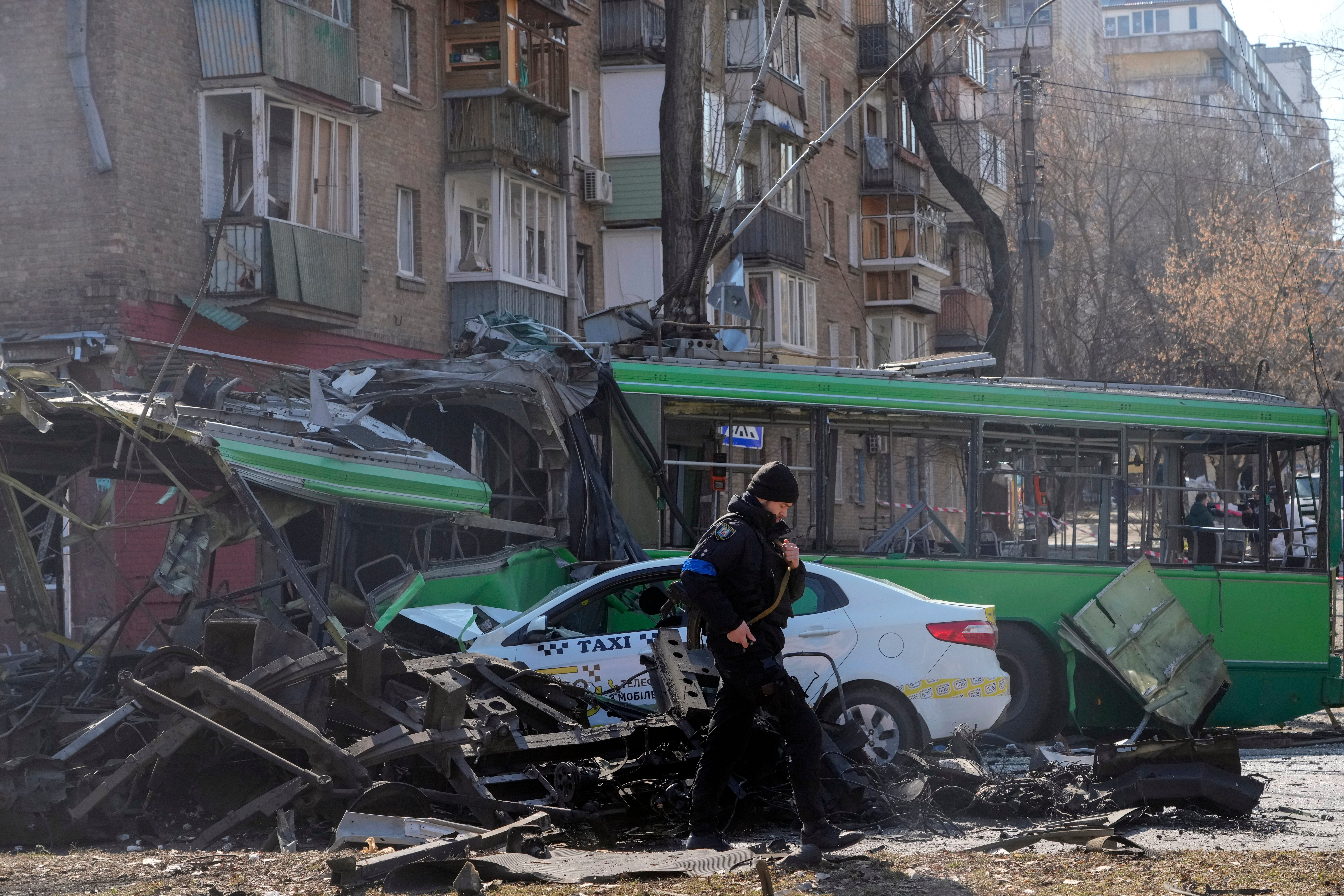 A Ukrainian soldier passes by a destroyed trolleybus and taxi after a Russian bombing attack in Kyiv on 14 March