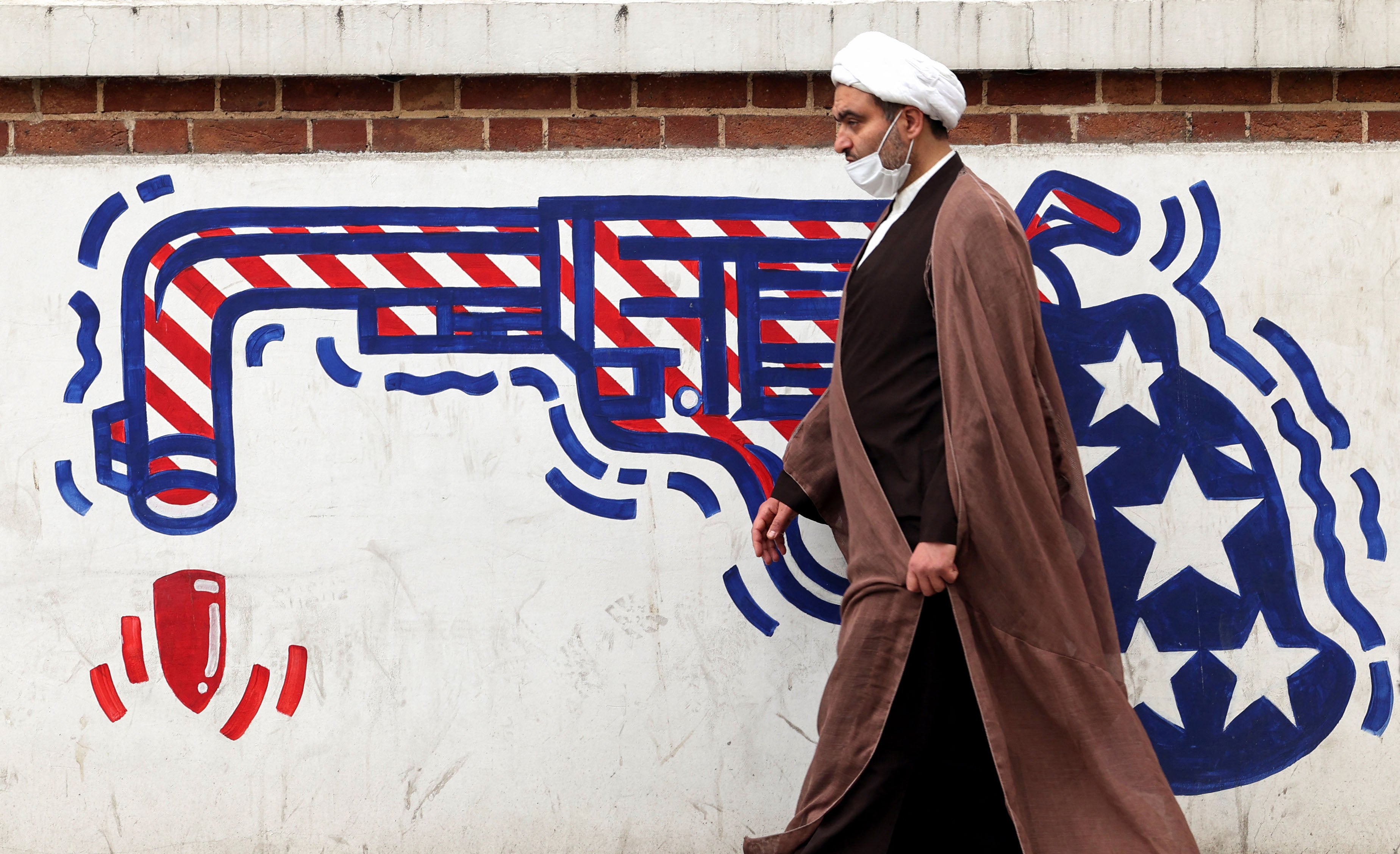 An Iranian cleric walks past an anti-US mural on a wall of the former United States embassy in Tehran