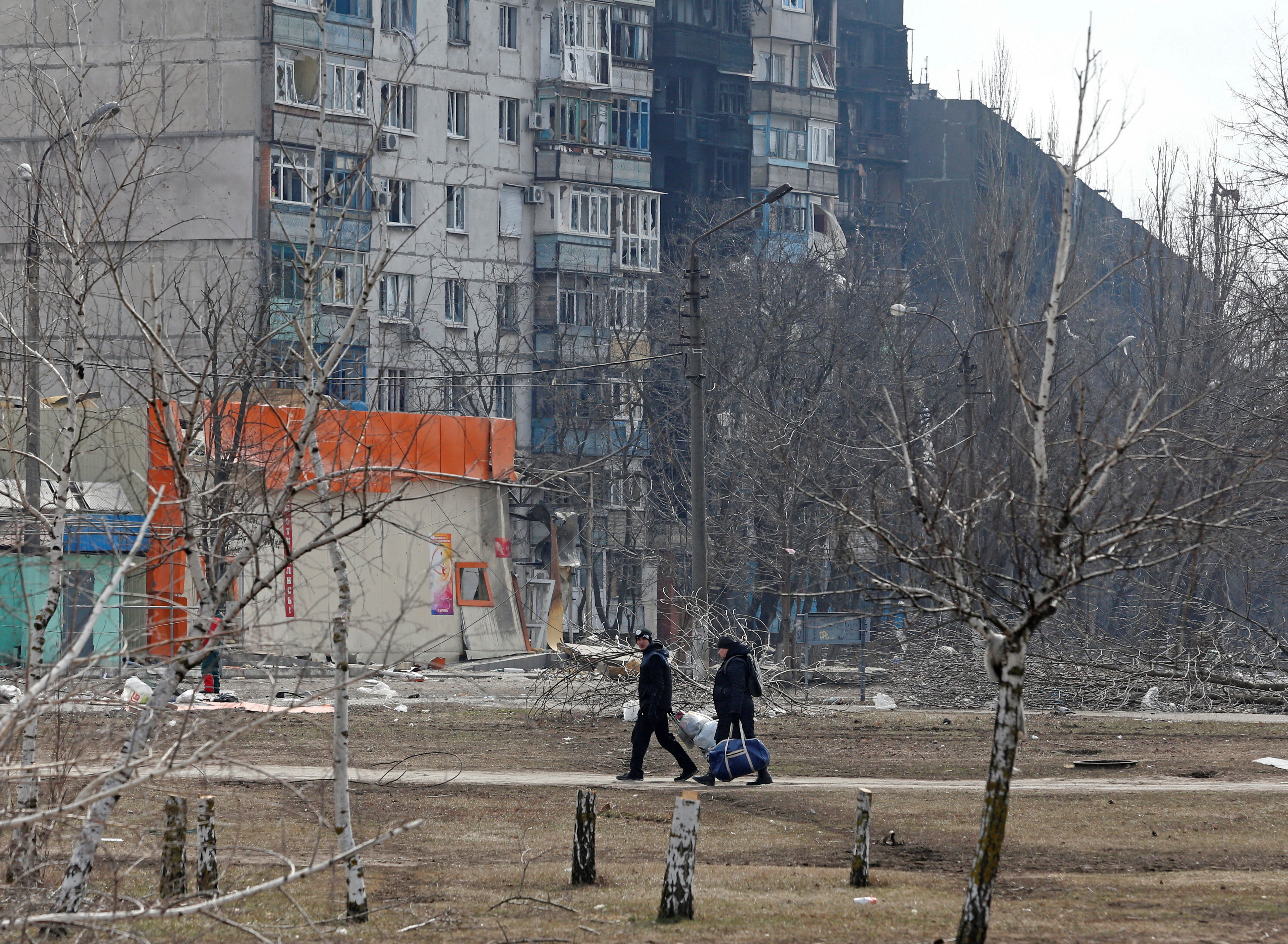 Local residents walk near a damaged residential building in the besieged southern port city of Mariupol