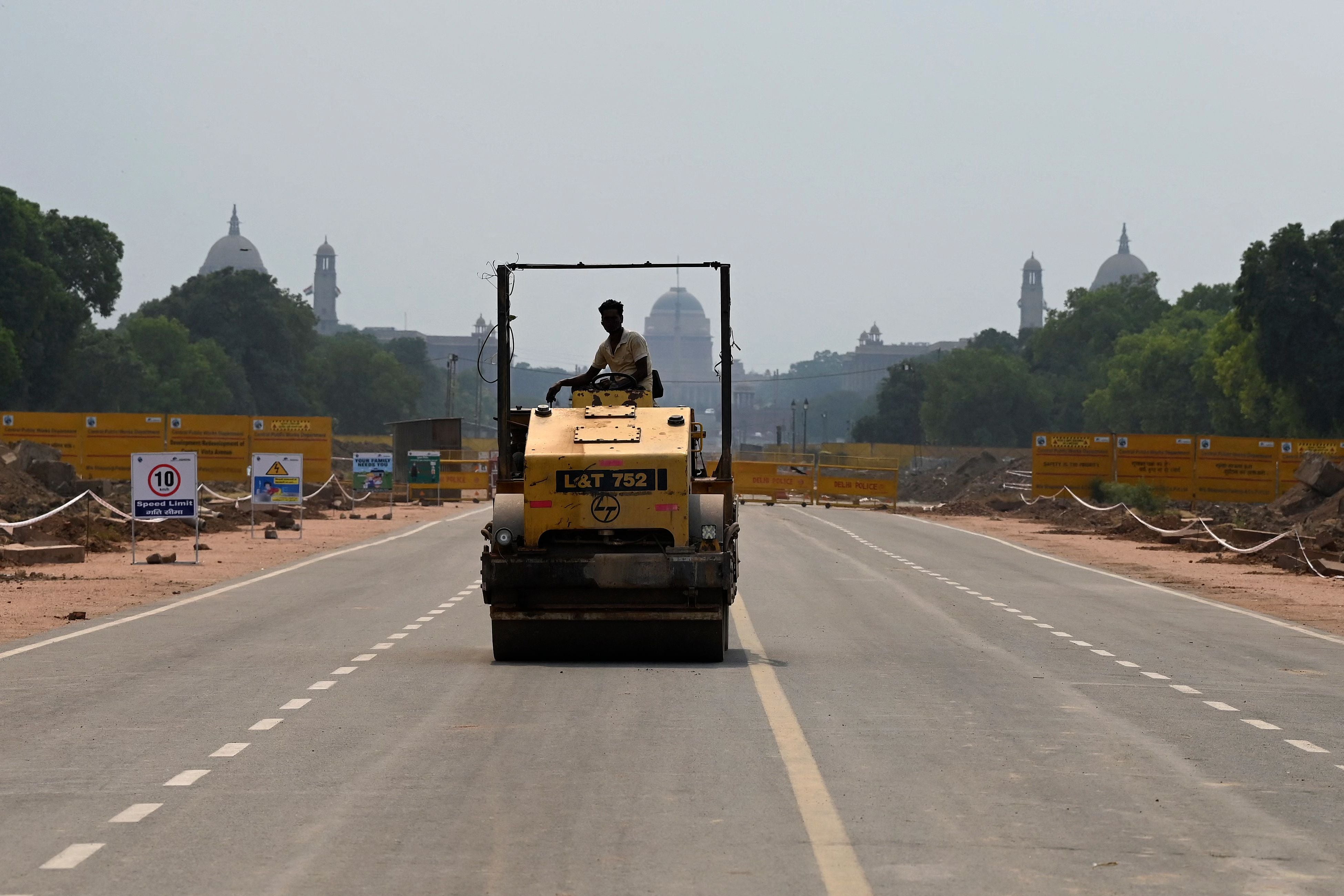 A worker rides a road roller along the Rajpath road next to the site of a redevelopment work of the Central Vista Avenue