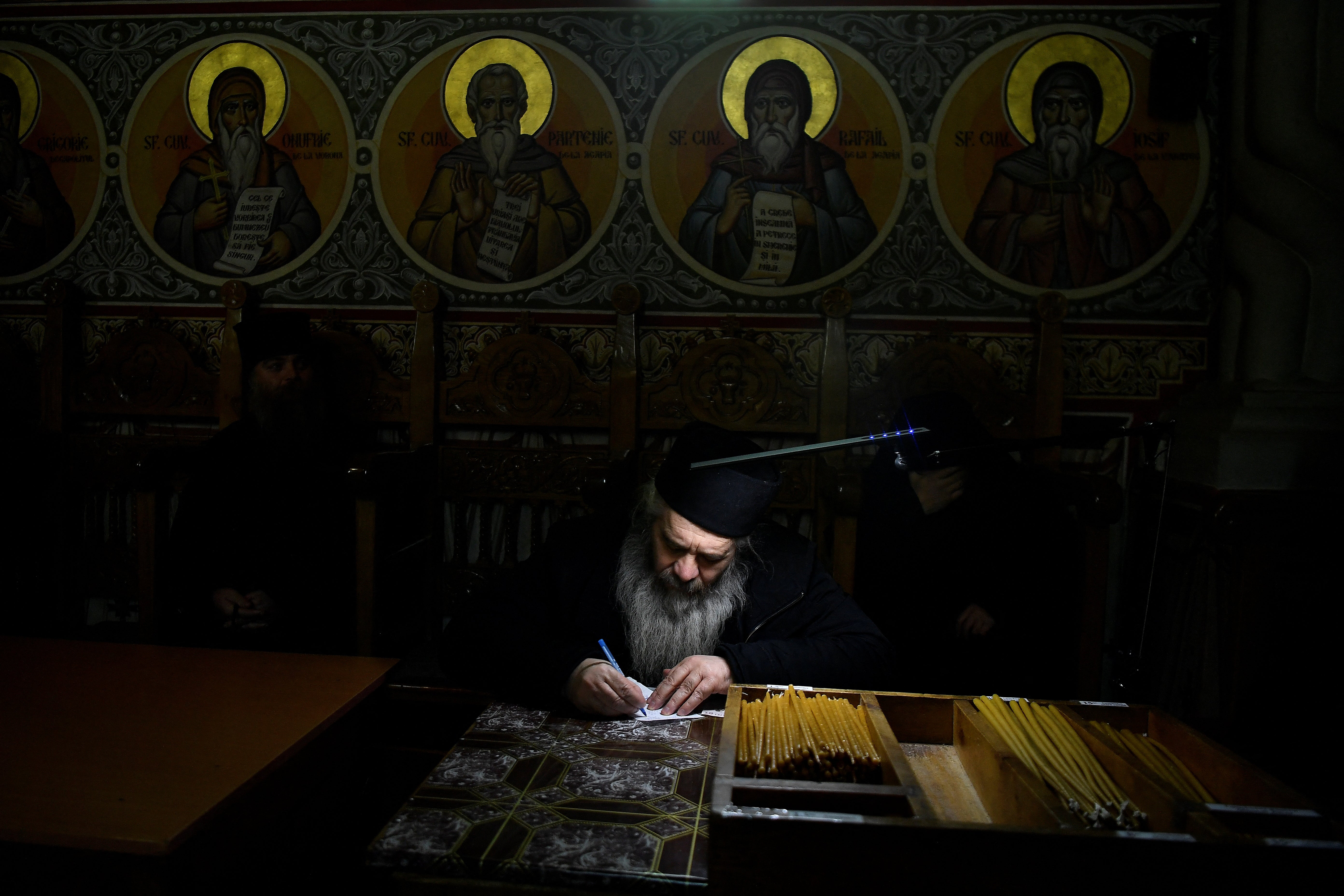 Father Caliopie takes lists of names of the dead and writes allocated prayer times for them, before service begins in the church at Putna monastery