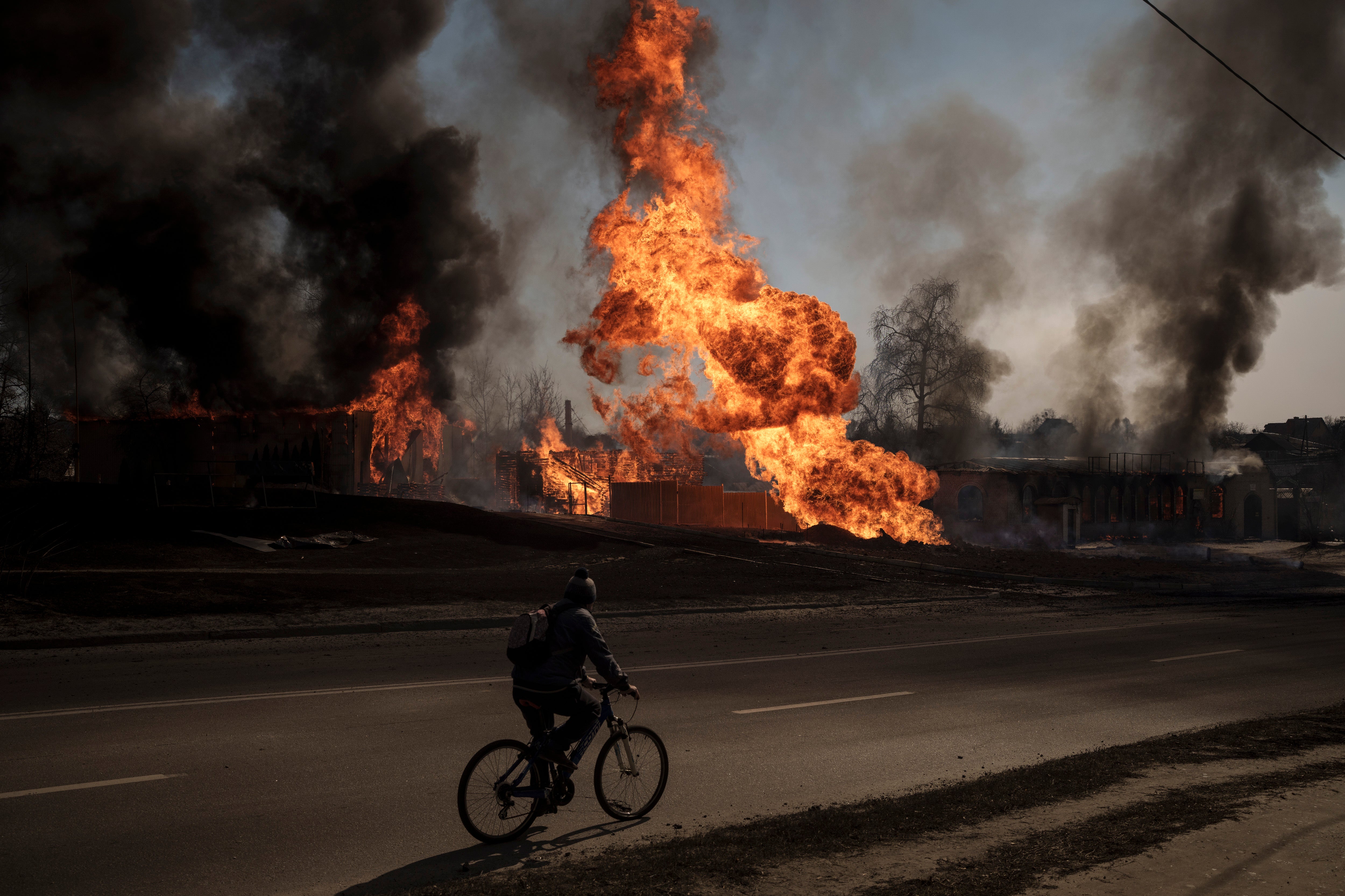 A man rides his bike past a fire following a Russian attack in Kharkiv, Ukraine