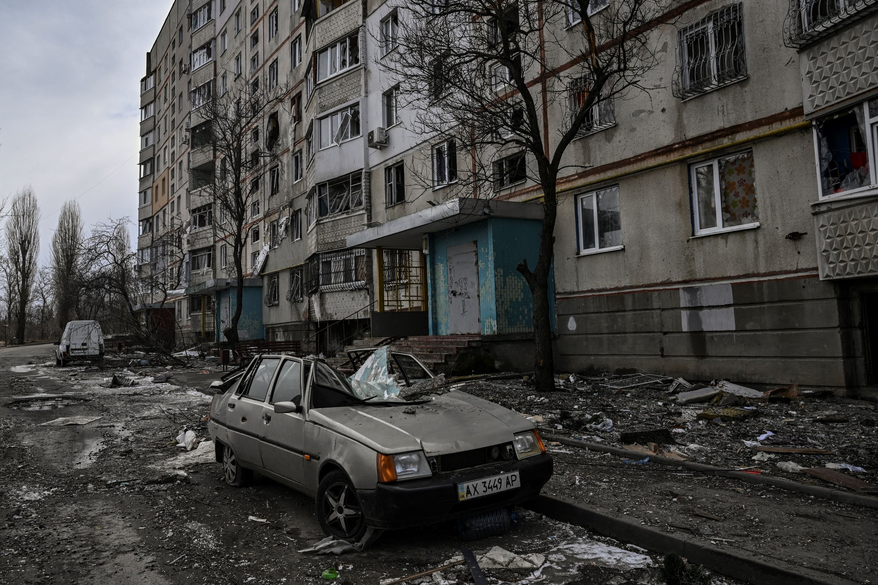 A destroyed car near a damaged apartment building in Kharkiv