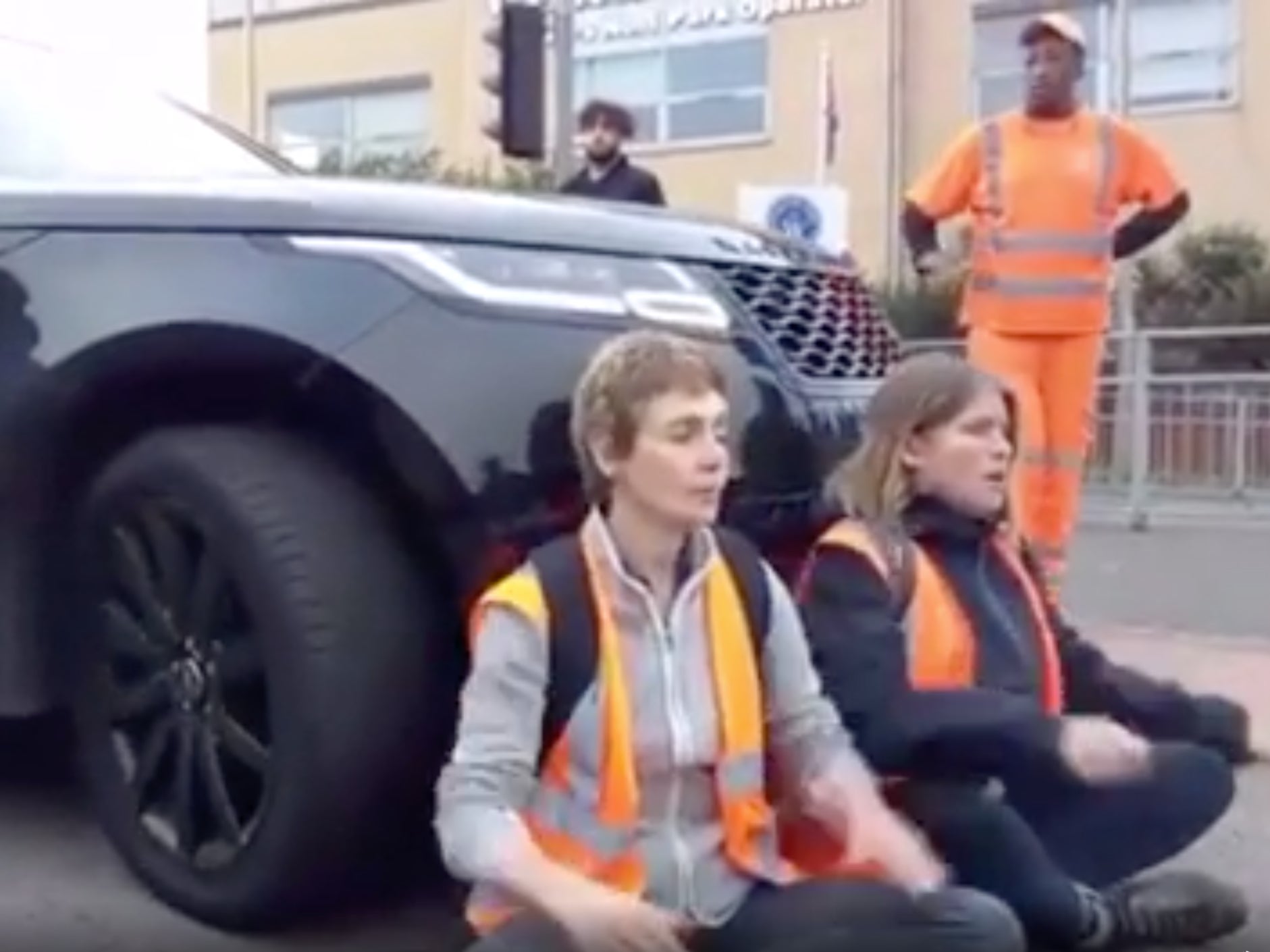 The car pulls forward while the protestors lean against the front of the vehicle