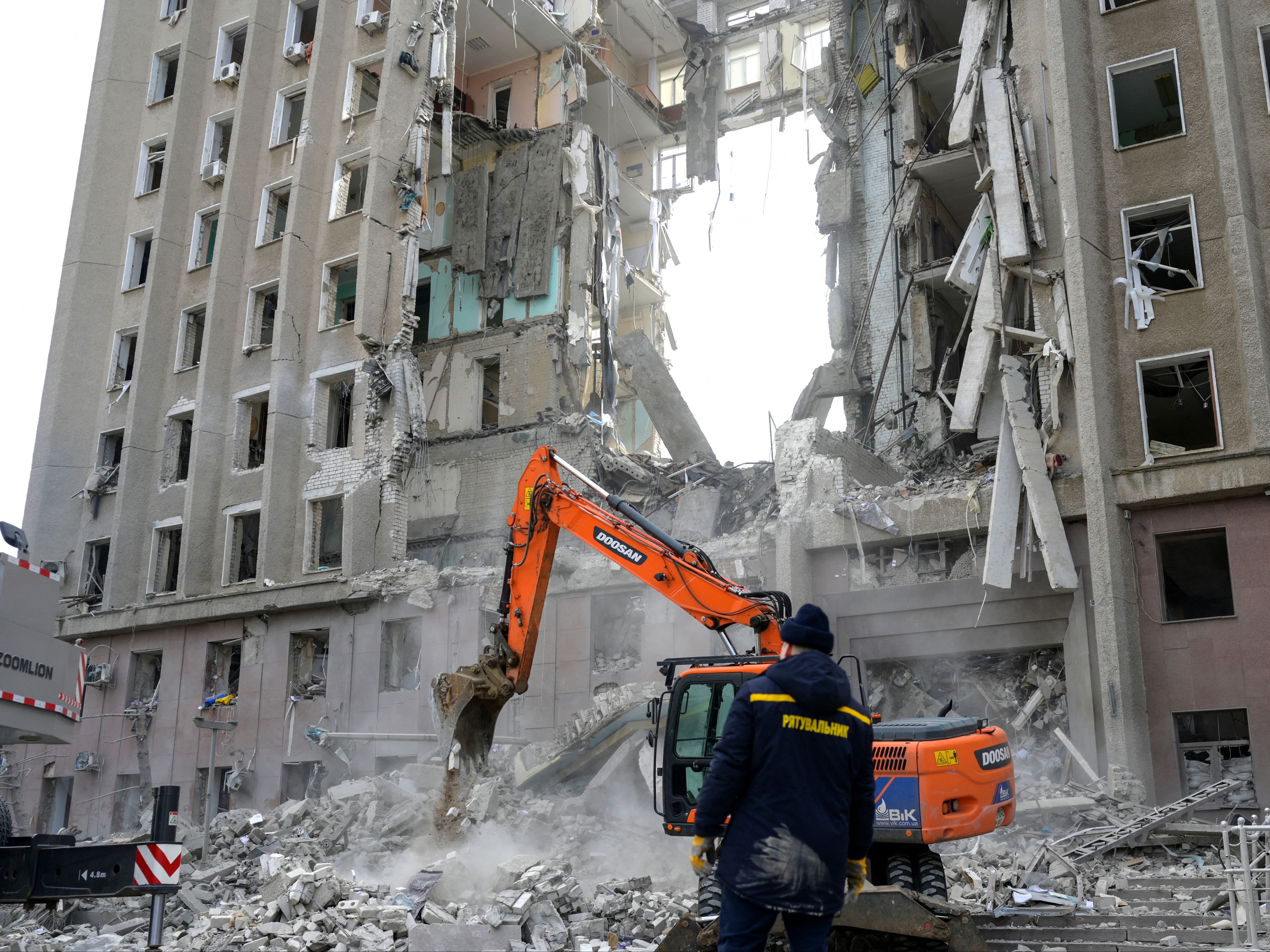 A worker watches an excavator clearing the rubble of a government building hit by Russian rockets in Mykolaiv in Ukraine