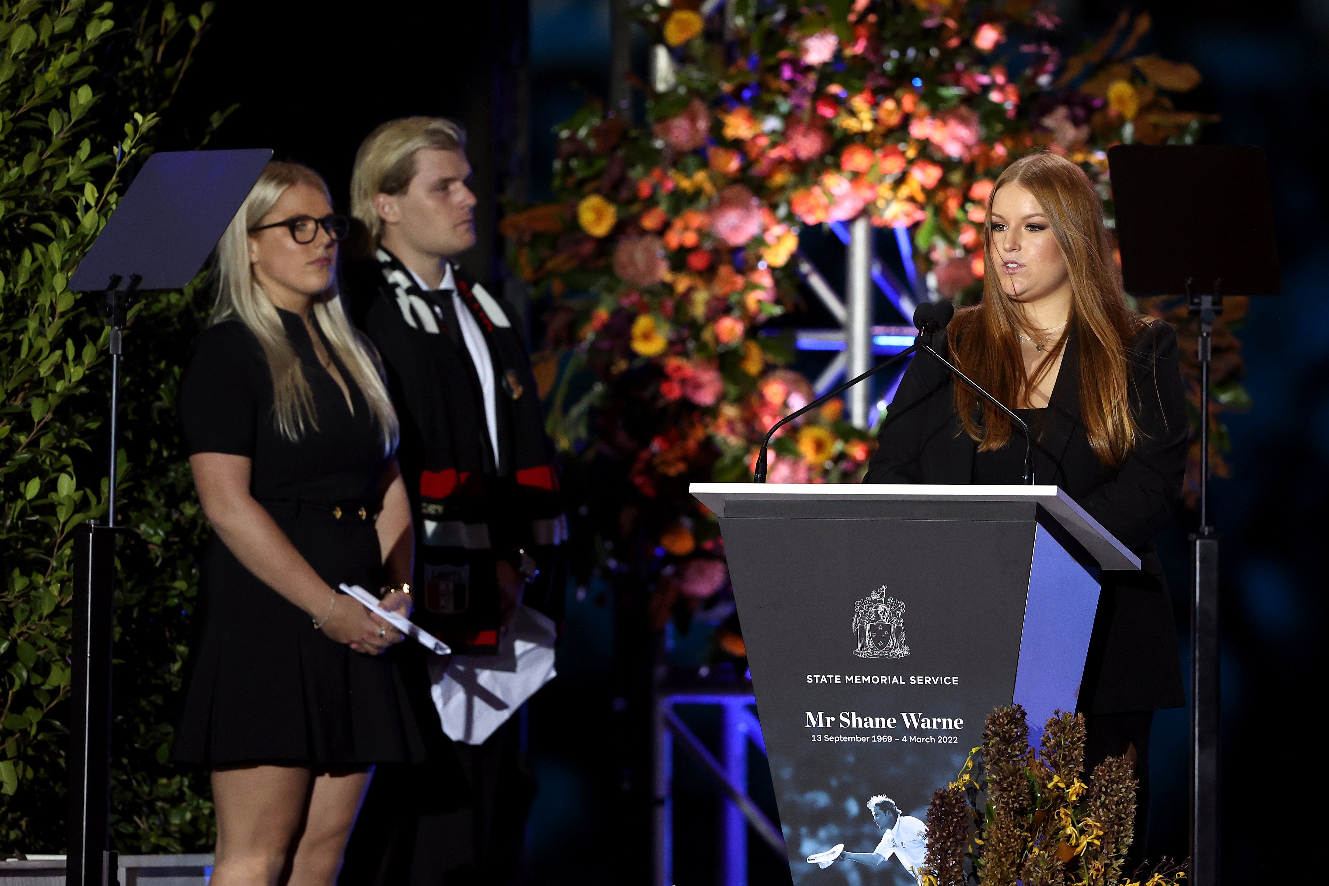 Summer Warne speaks on stage alongside Jackson Warne and Brooke Warne during the state memorial service