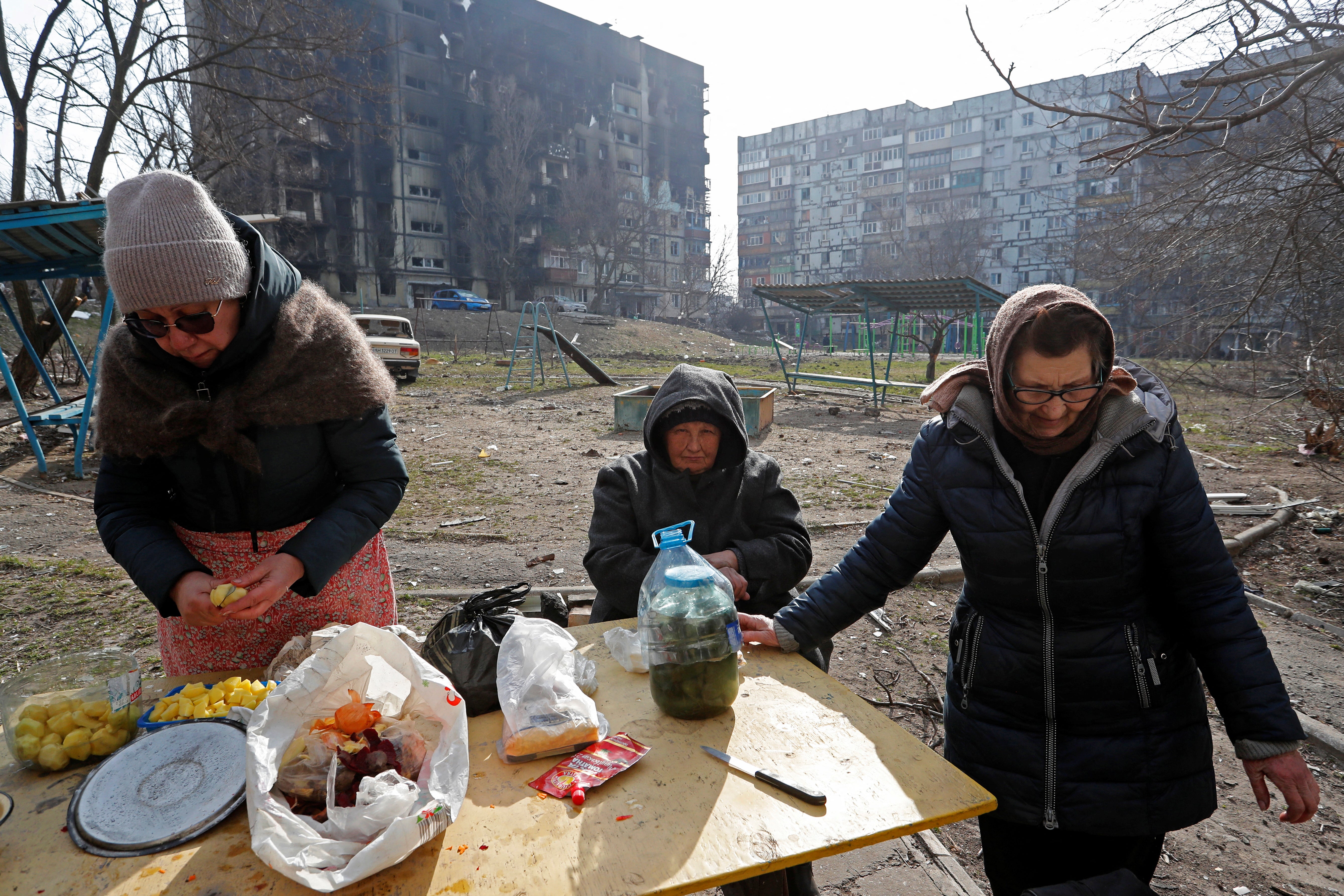 Local residents cook food outside an apartment building damaged during Ukraine-Russia conflict in the besieged southern port city of Mariupol