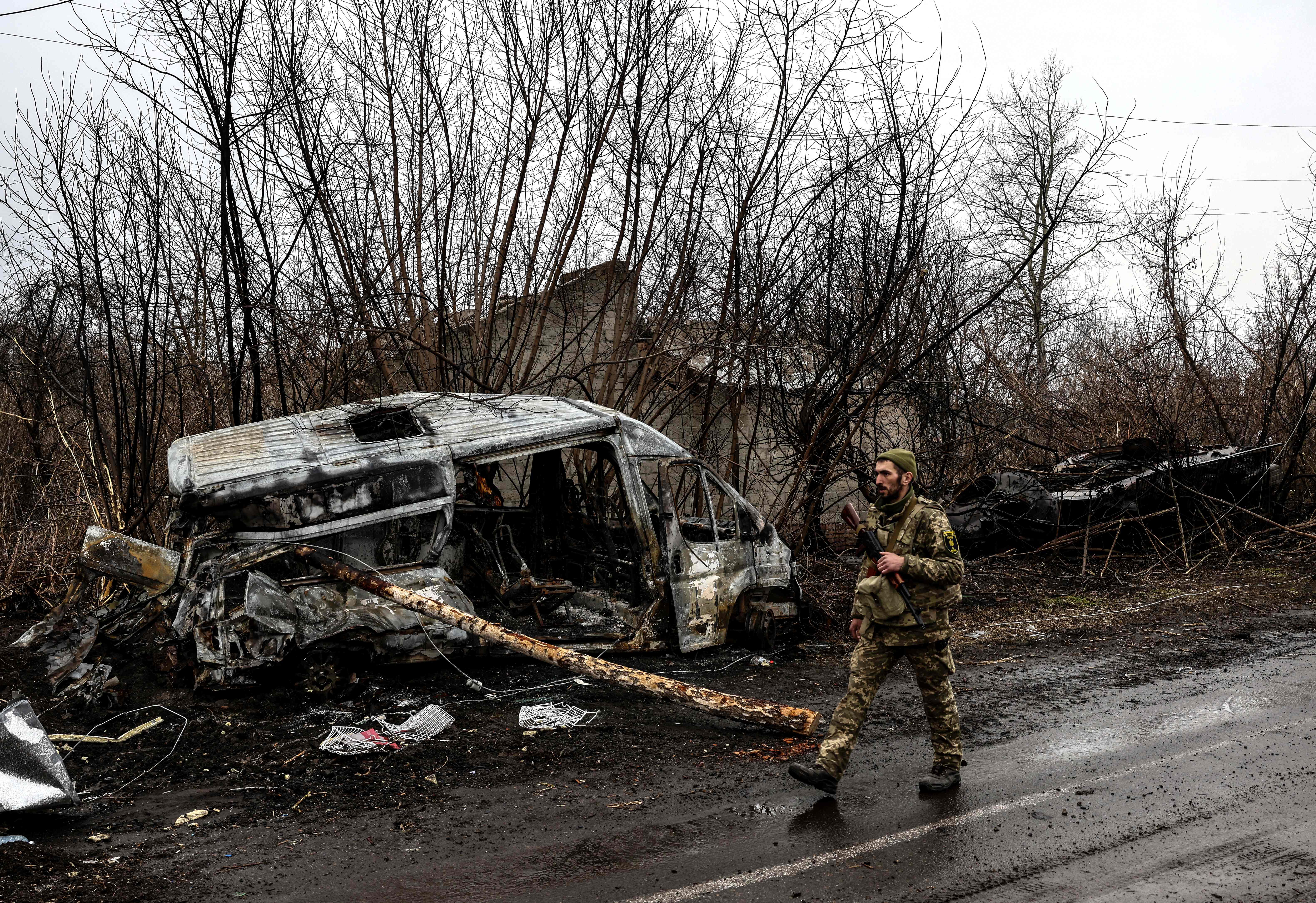 A Ukrainian soldier patrols next to a burned vehicle in the village of Lukianivka near Kyiv on Wednesday