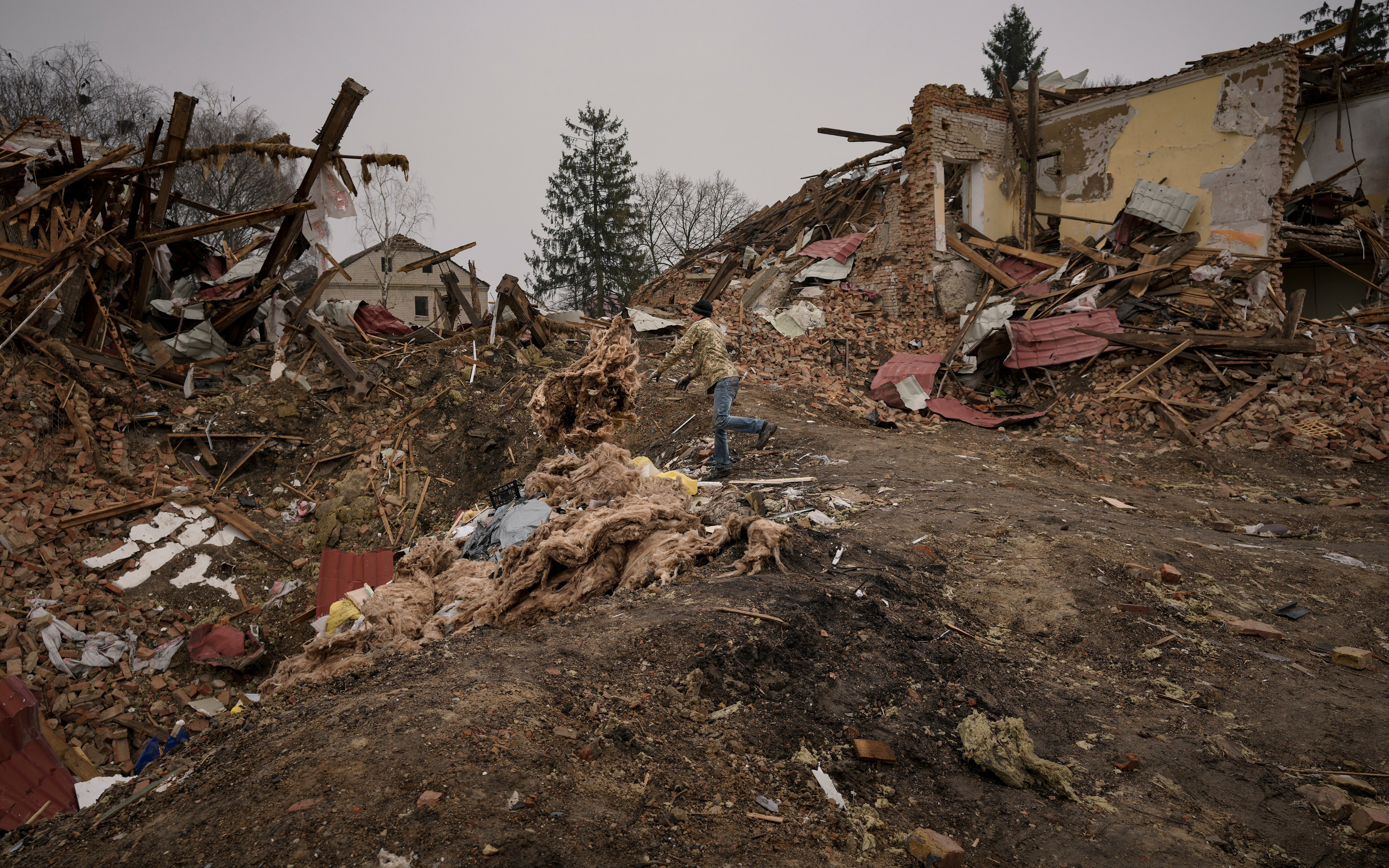 A man throws debris from buildings destroyed during fighting between Russian and Ukrainian forces in a large explosion crater outside Kyiv